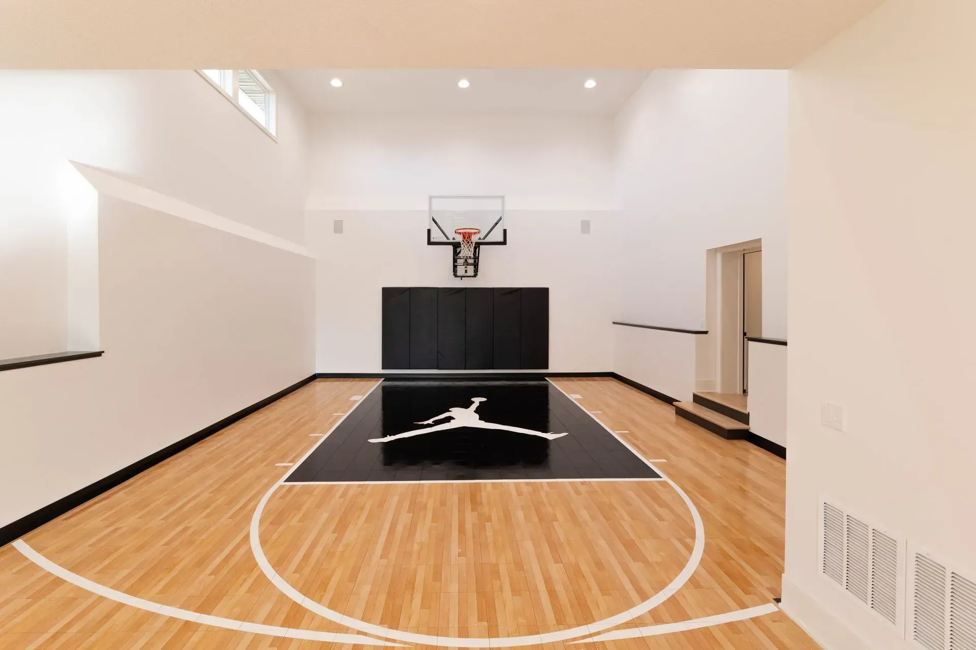 Indoor basketball court with Jordan logo at center. Black and white color scheme, wooden floor, hoop, and backboard.