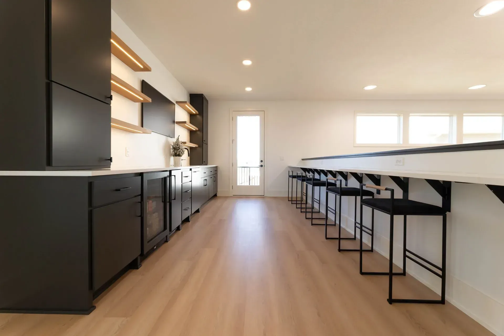 Modern kitchen with black cabinets, white countertops, and wood flooring; a long island with bar stools.