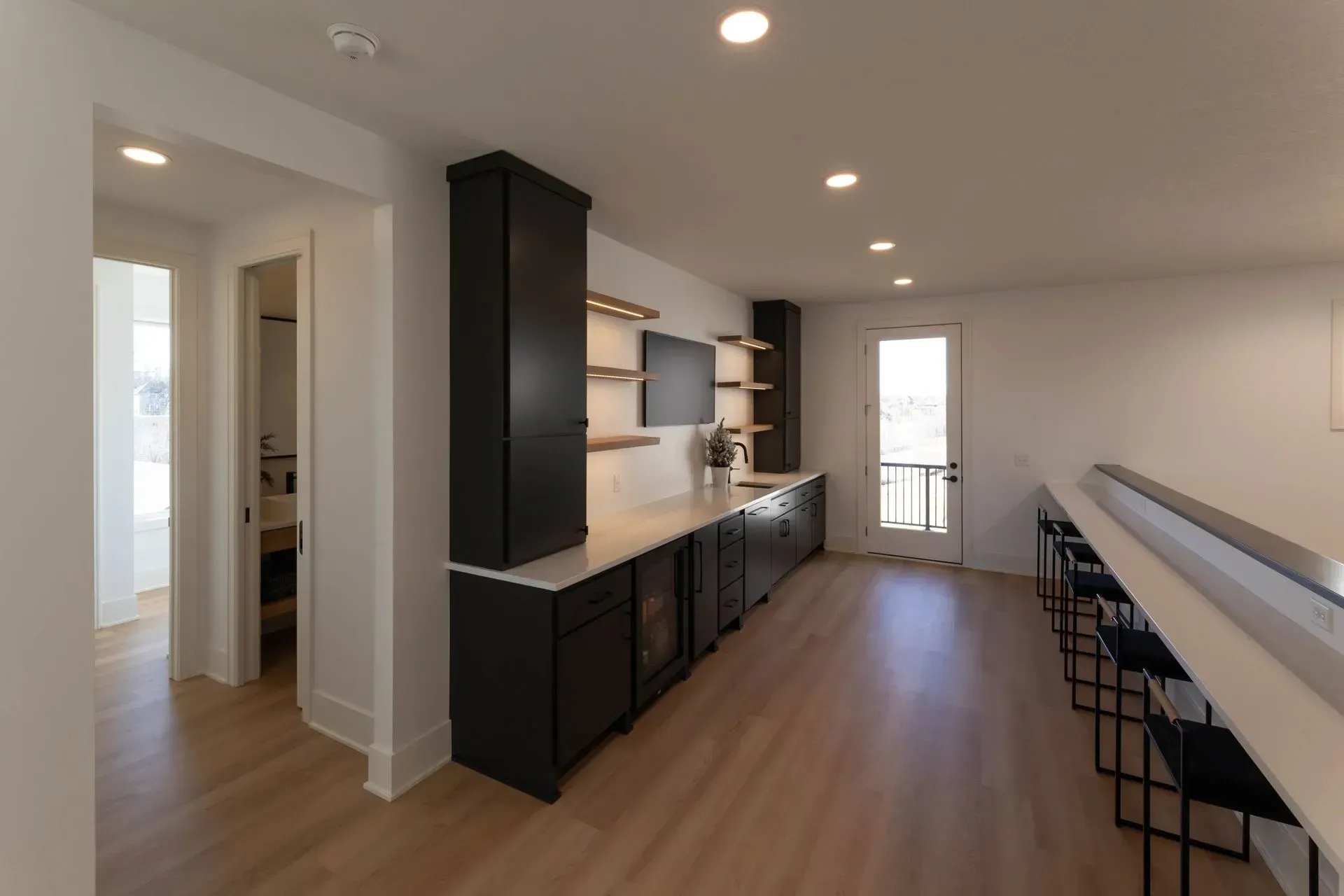 Interior with a black wet bar, light wood floor, and hallway leading to a bathroom.