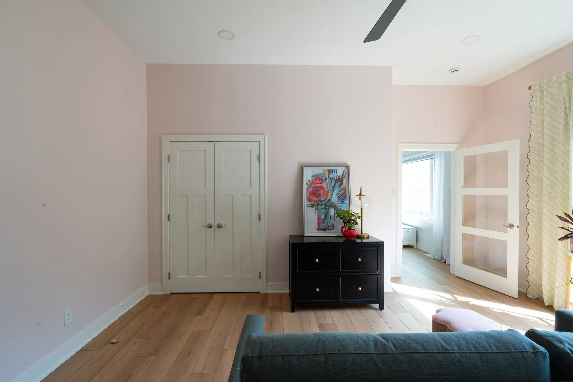 Living room with pink walls, wood floors, black dresser, and a doorway.