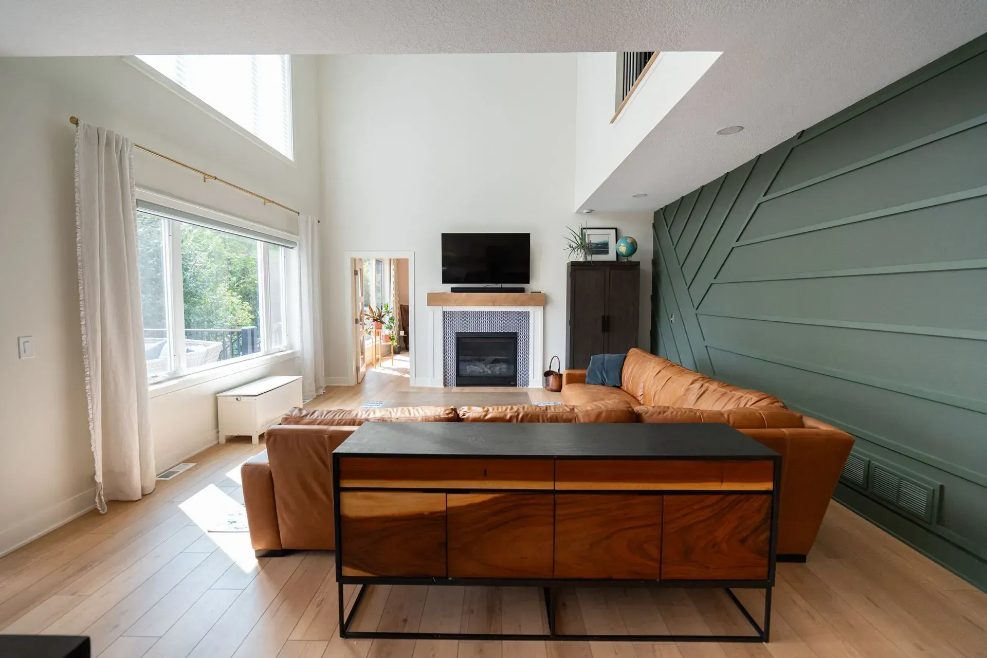 Modern living room with leather couch, teal accent wall, fireplace, and wooden cabinet.
