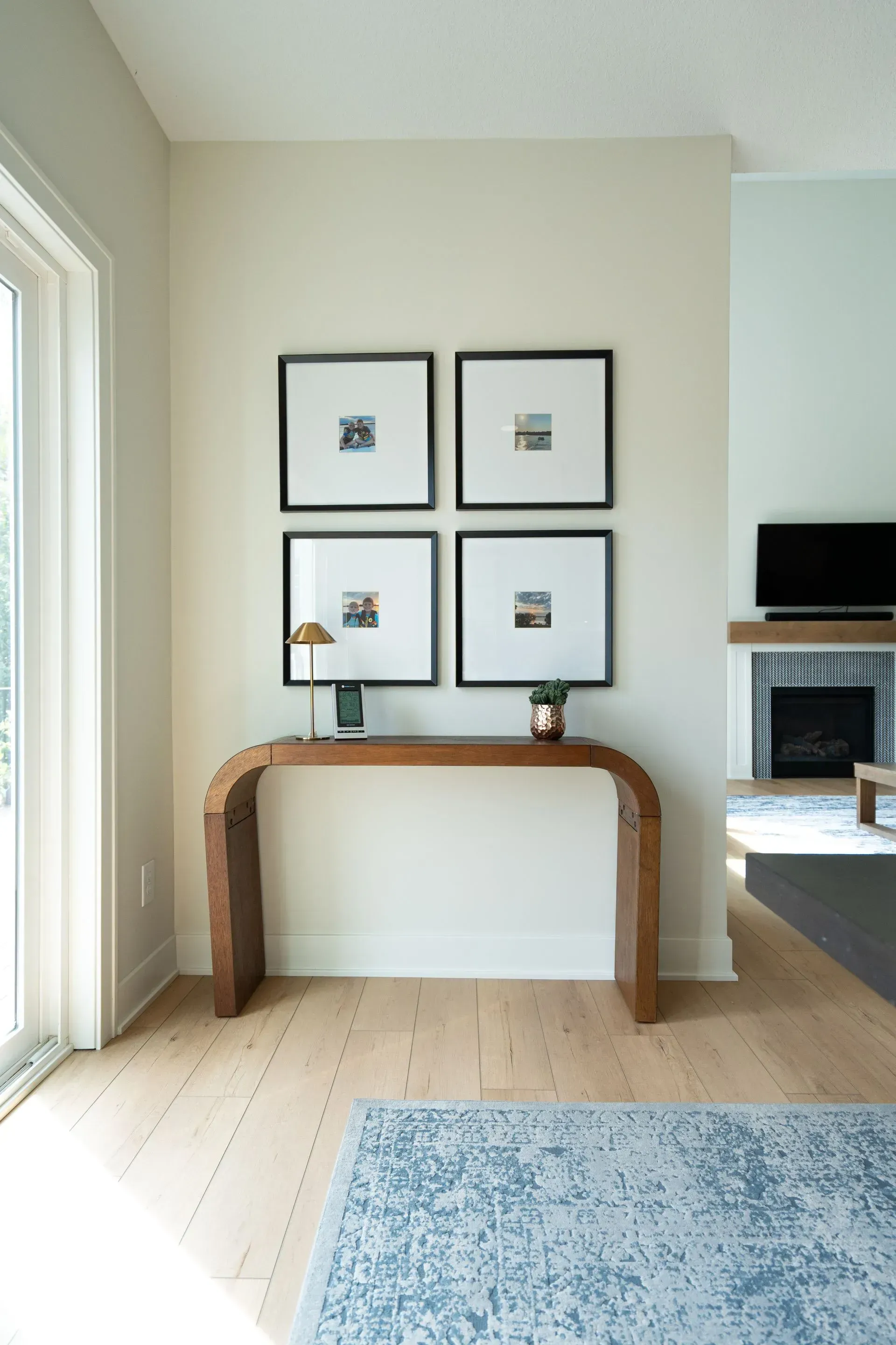 Wooden console table beneath four framed photos, a lamp, and a rug in a bright room.