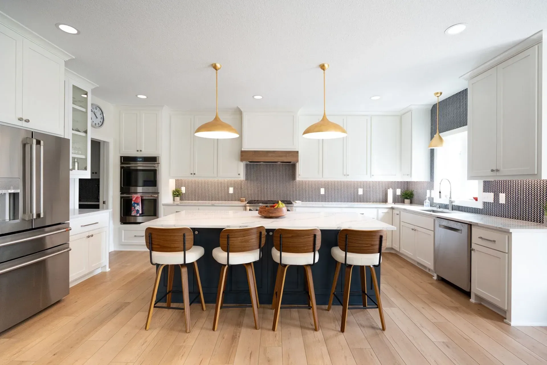 Modern kitchen with white cabinets, dark blue island, gold pendant lights, and wooden floors.