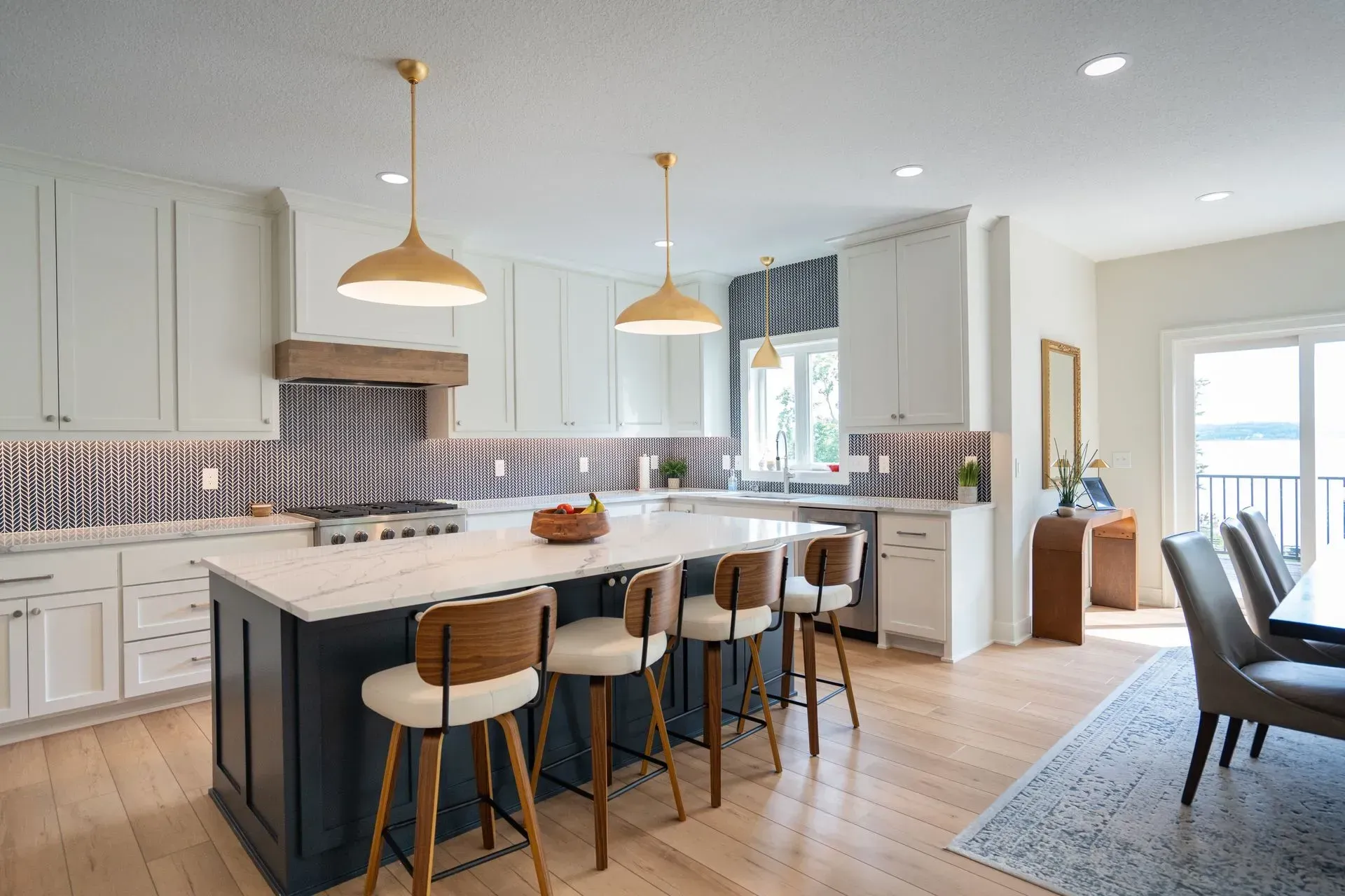 Spacious kitchen with a dark blue island, white cabinets, light wood floors, and gold pendant lights.