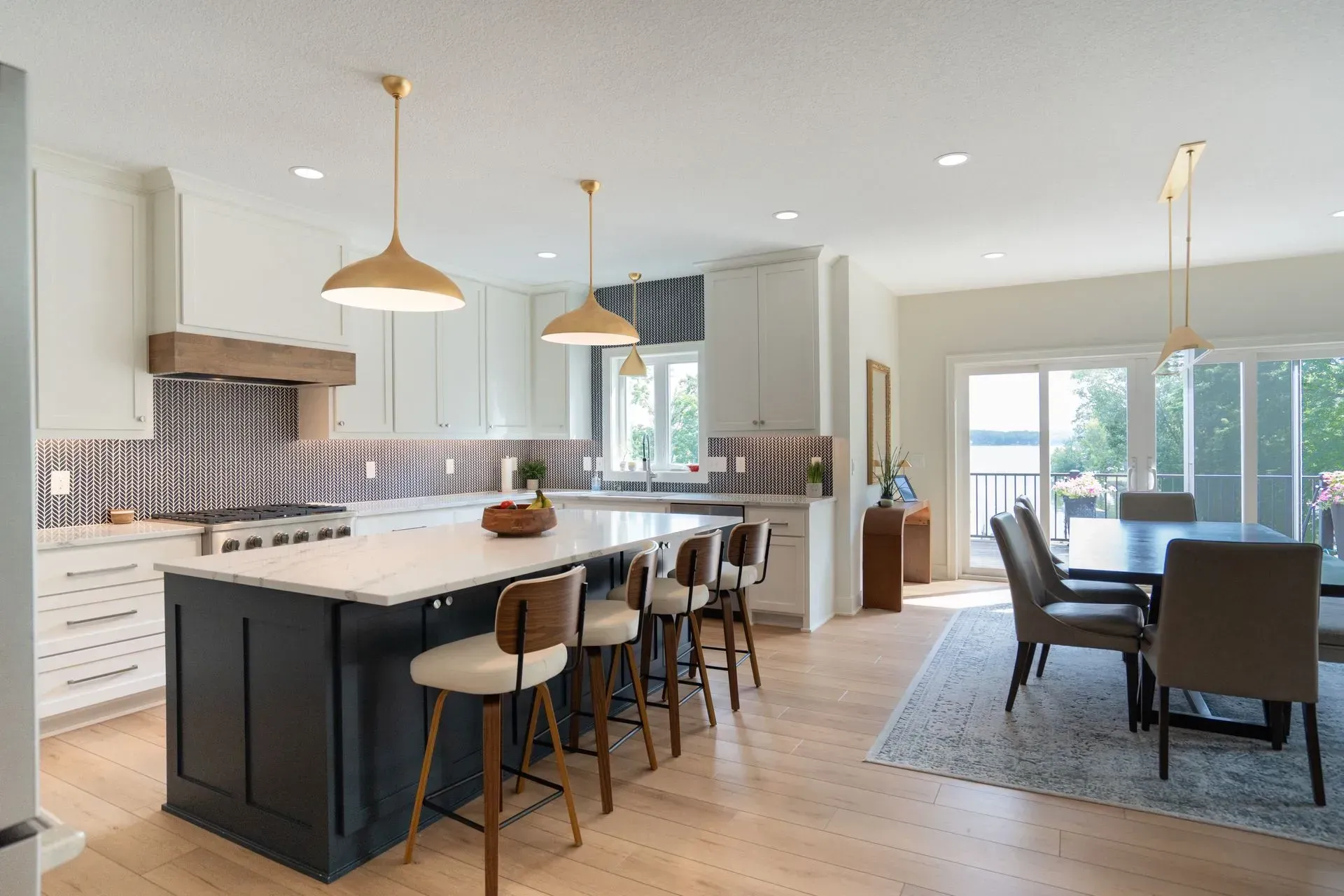 Kitchen with island, dining area, and outdoor view. Brass pendants, blue and white backsplash, dark island with seating.