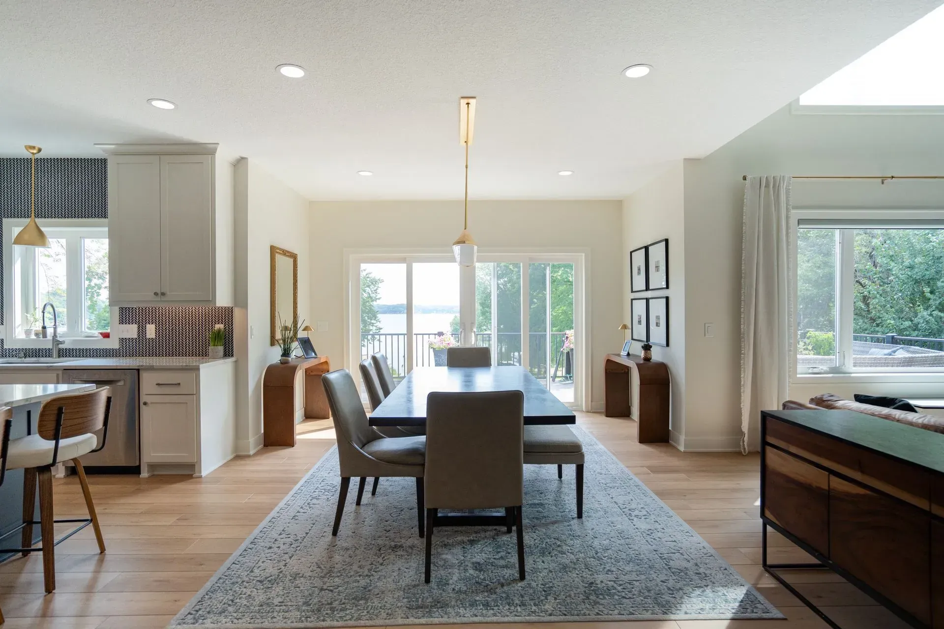 Open-plan dining and kitchen with wood floors, long table, and a view of a body of water.