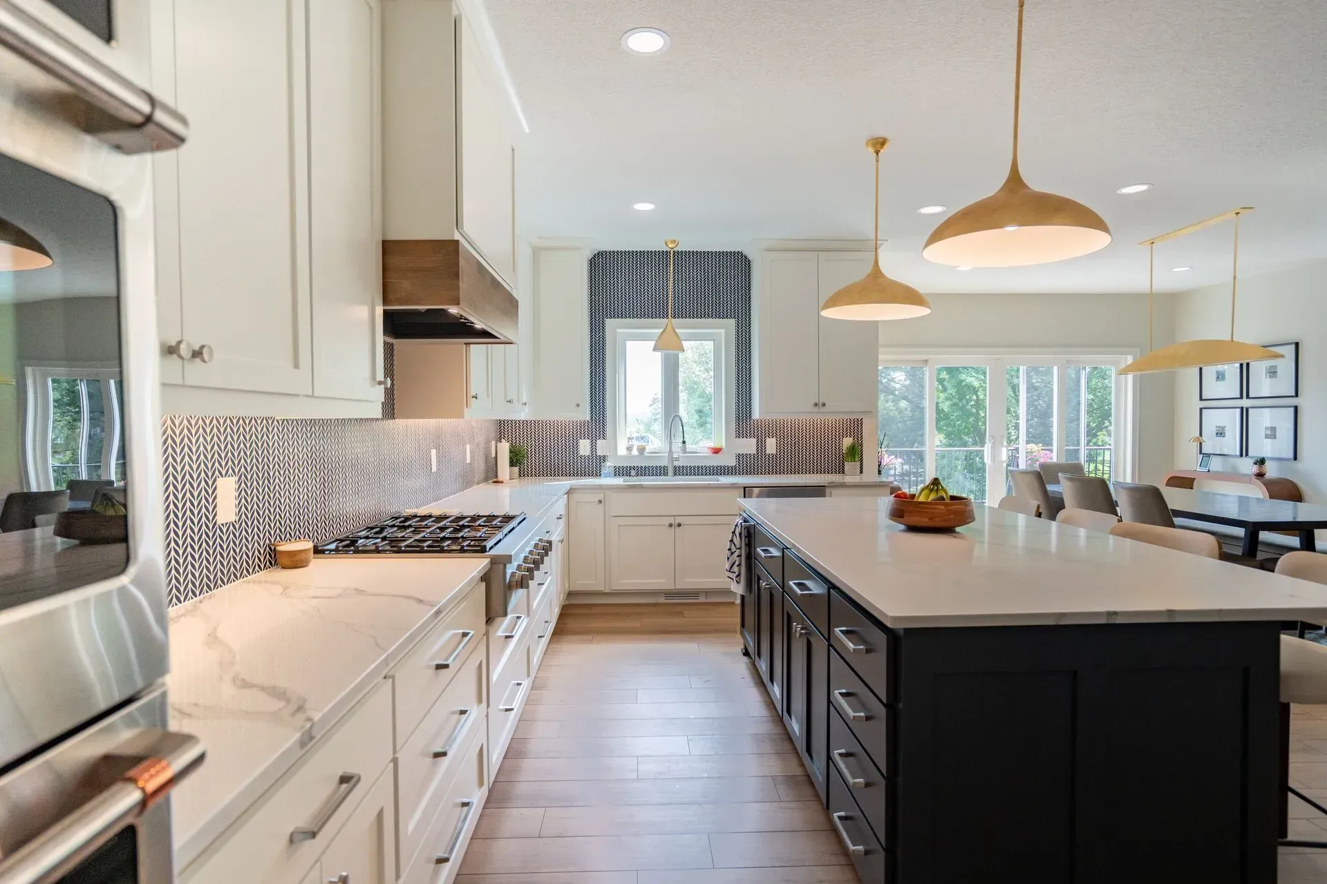 Modern kitchen with white and dark cabinetry, marble countertops, and gold pendant lights.