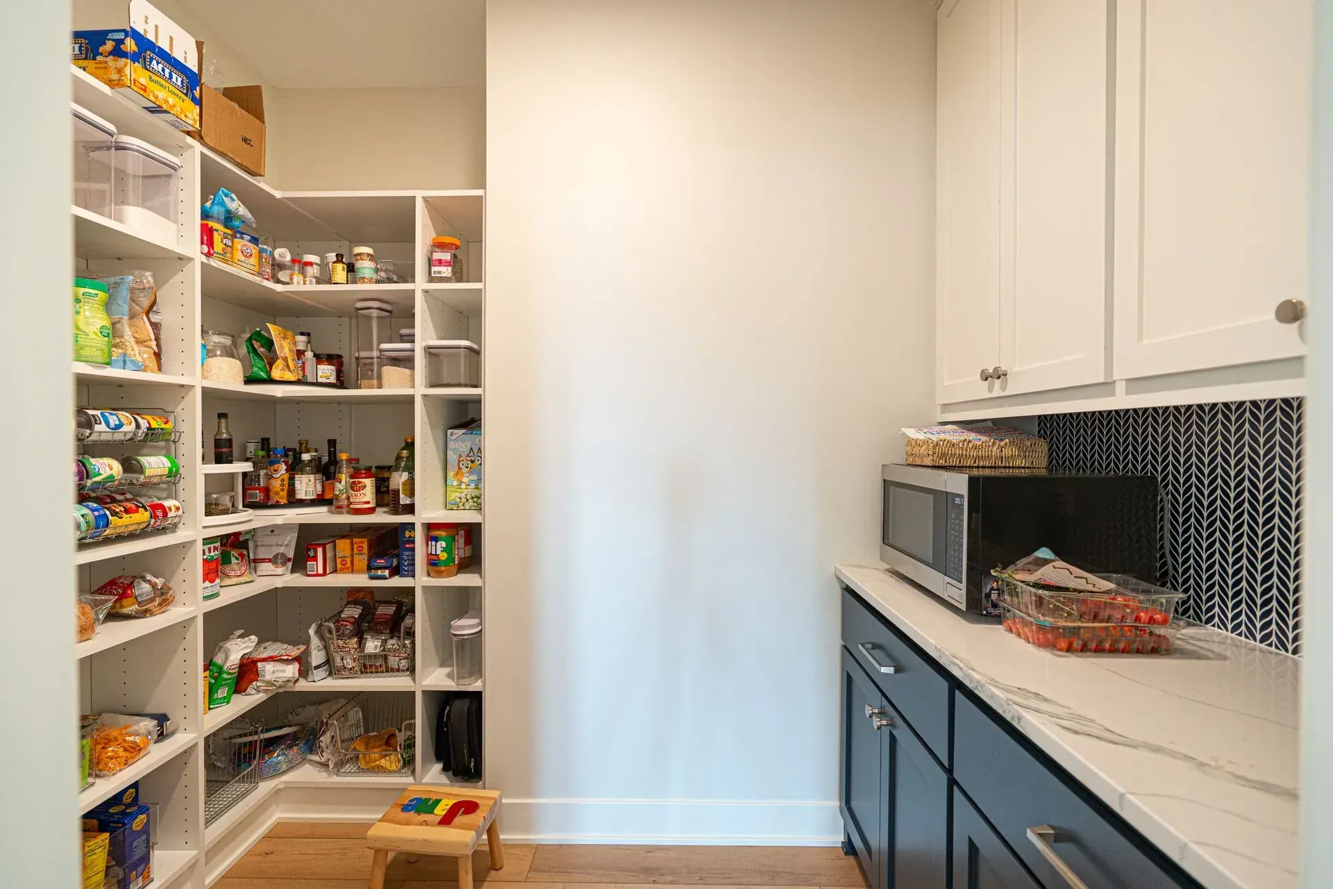 Pantry with shelves of food, and cabinets with a microwave. White and blue color scheme.