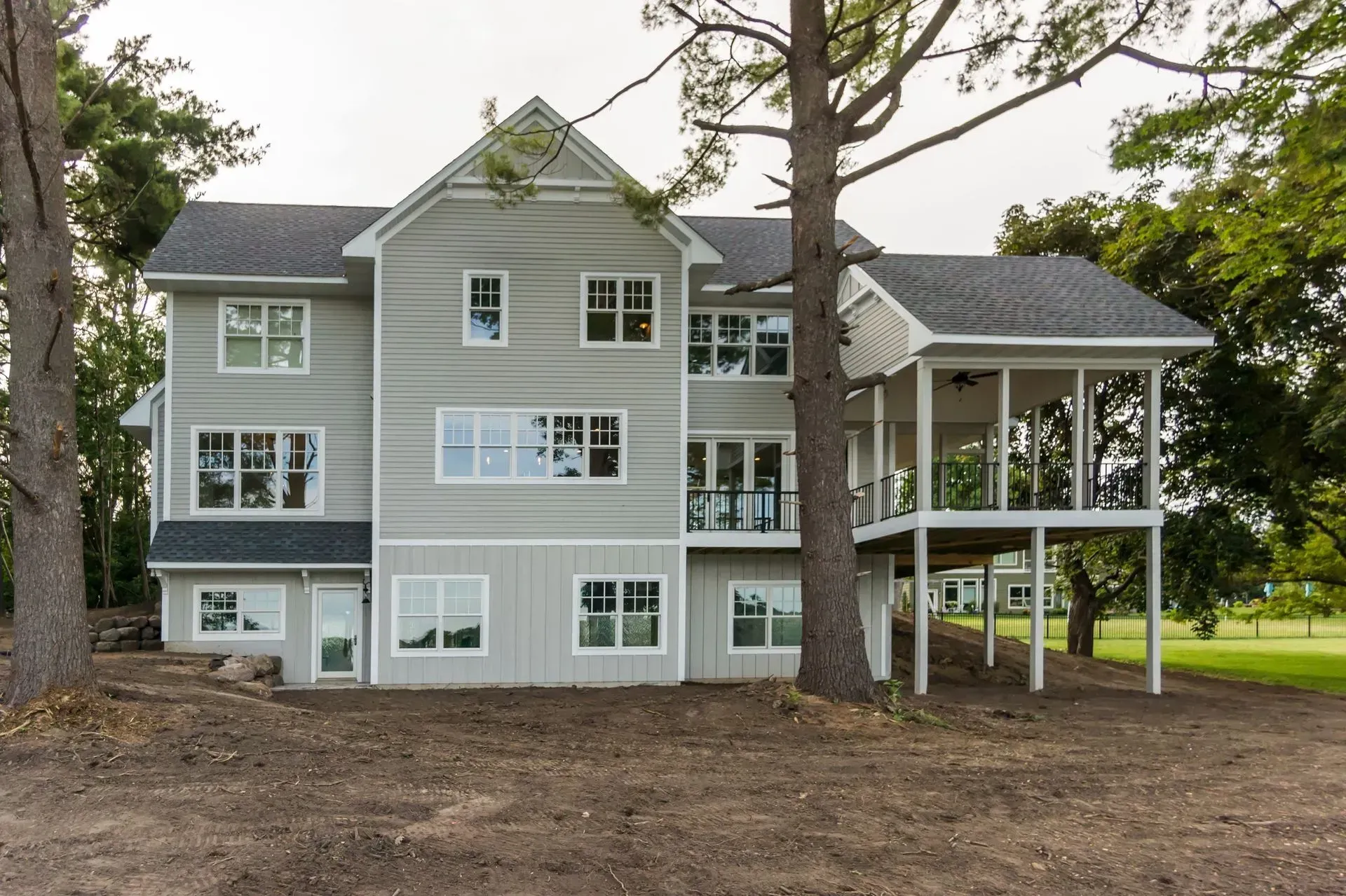 Gray two-story house with screened porch, surrounded by trees and a grassy lawn.