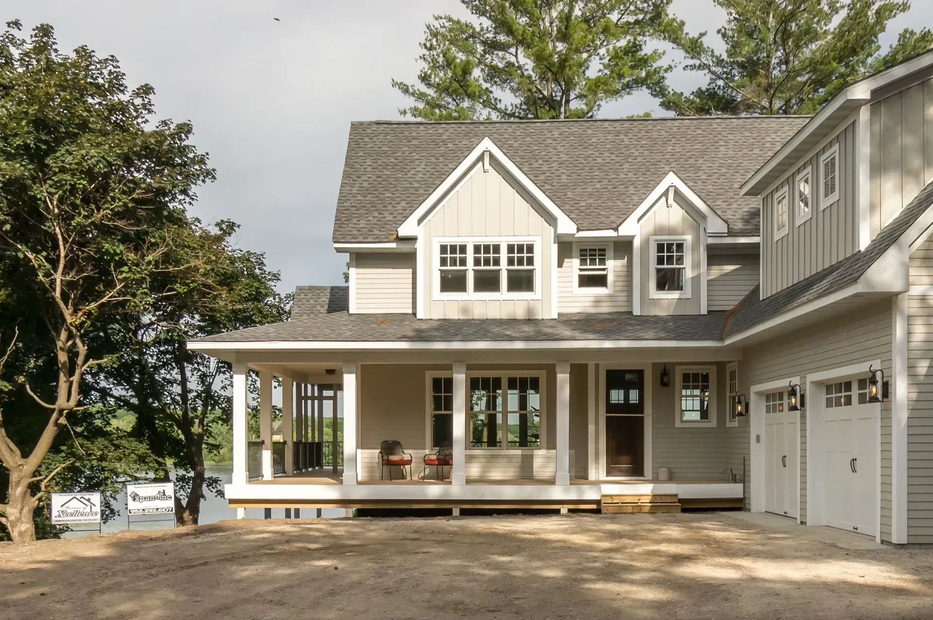 Two-story house with light gray siding, a porch, and a garage; trees in the background.