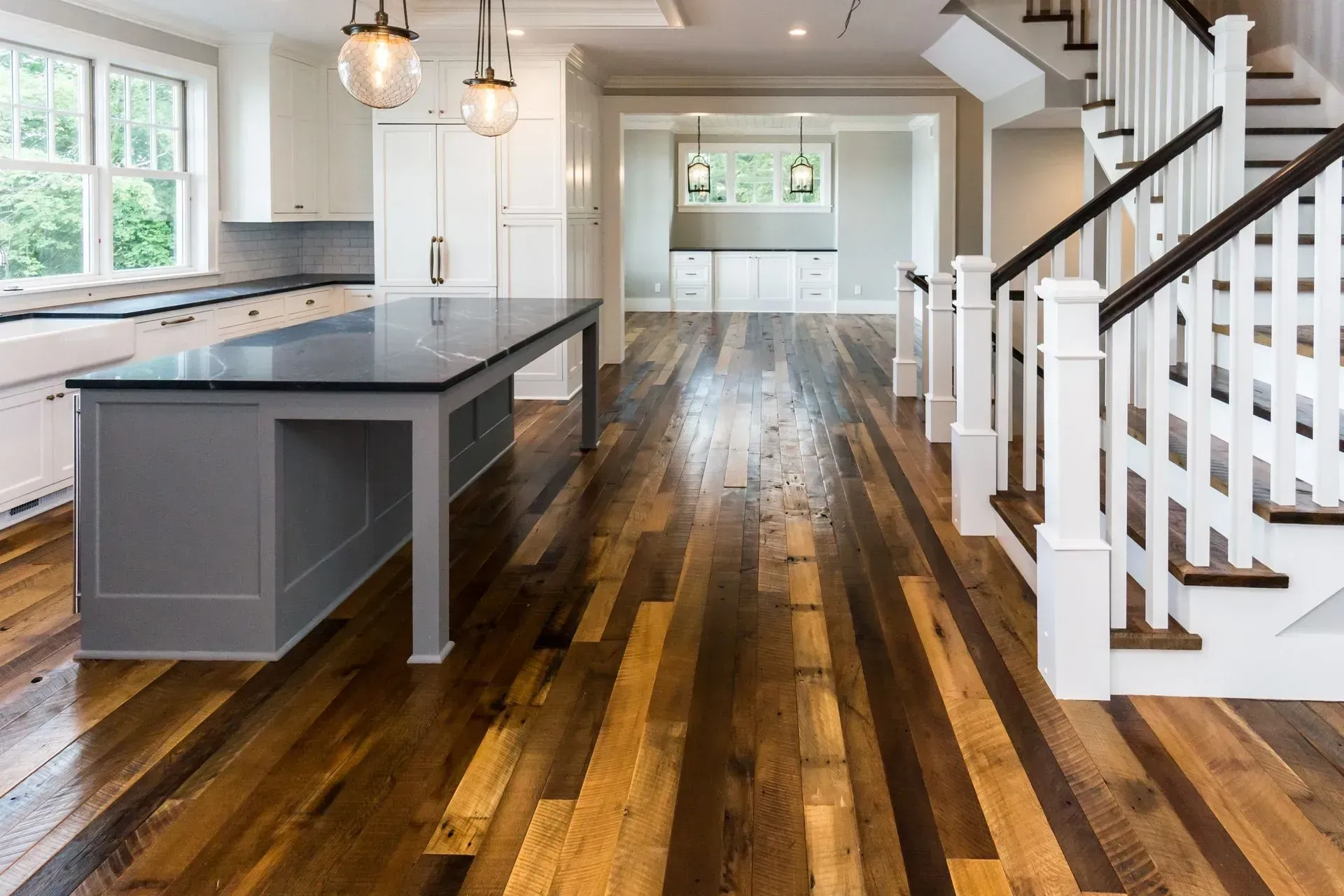 Kitchen with wooden floor, island, white cabinets, and stairs.