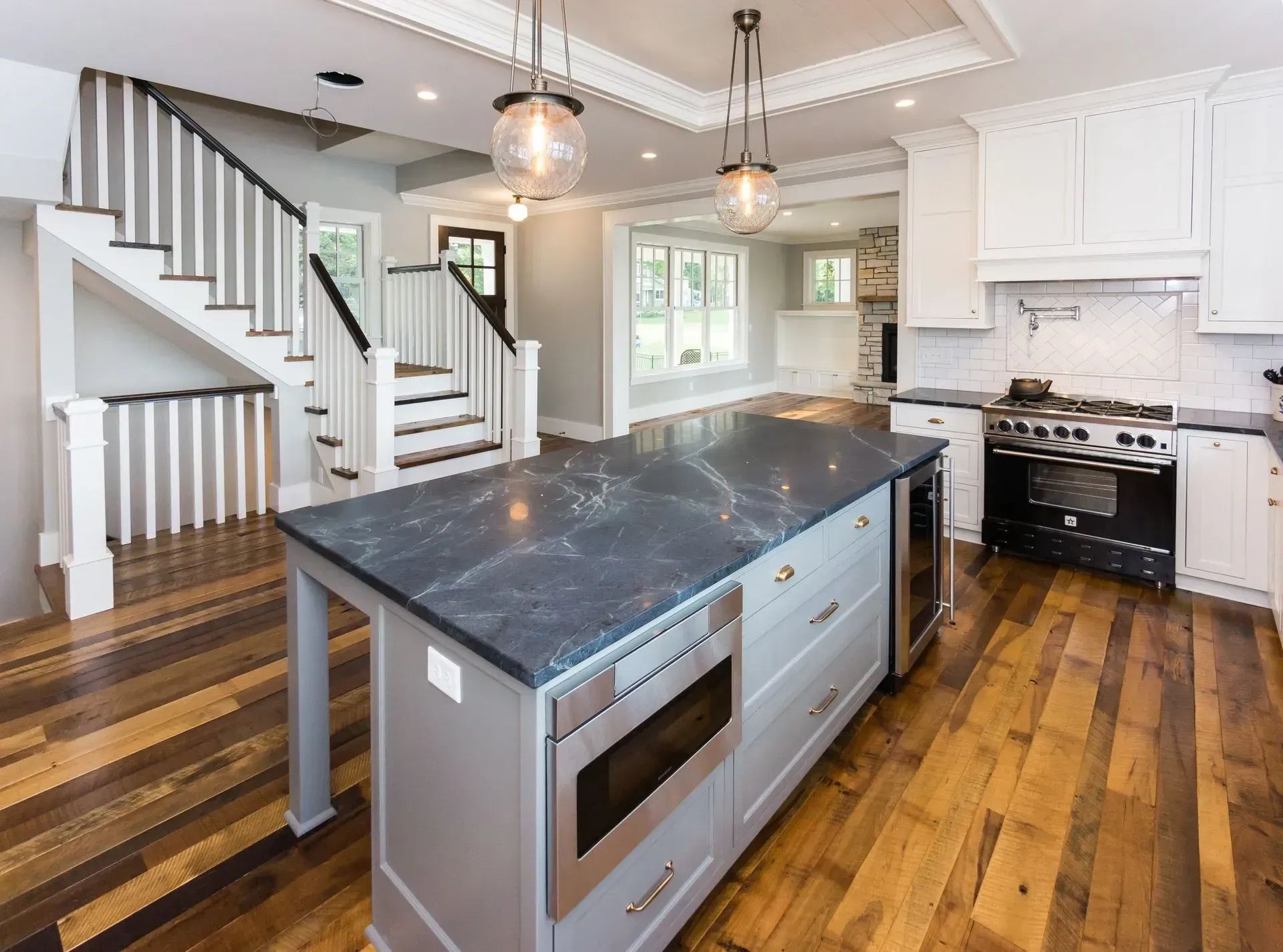 Kitchen with large island, stainless steel appliances, hardwood floors, and stairs.