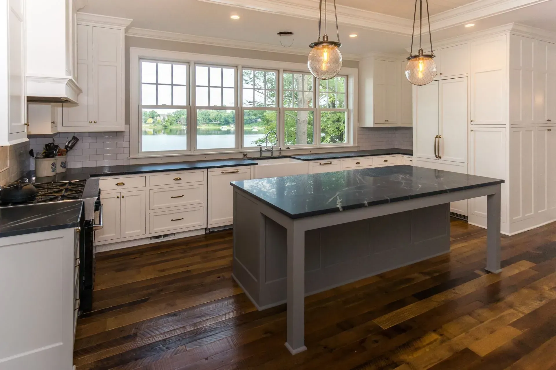 Kitchen with white cabinets, dark countertops, gray island, and view of water through windows.