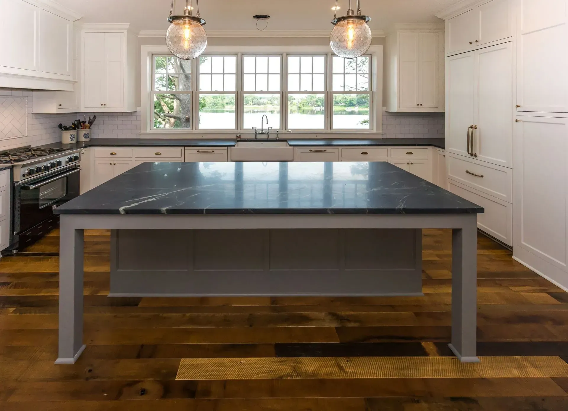 Kitchen with white cabinets, dark gray island, wood floors, and window.