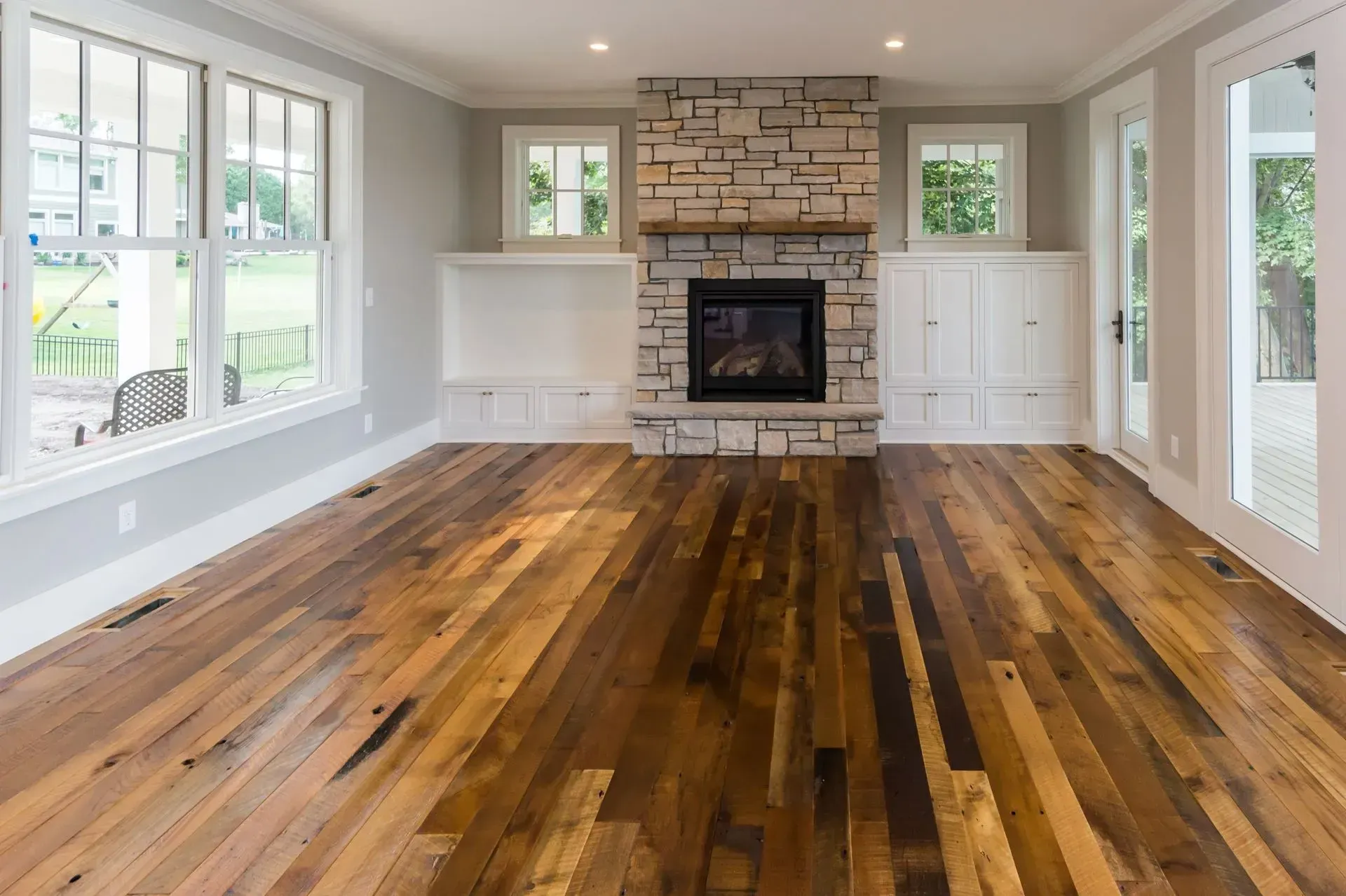Living room with hardwood floor, stone fireplace, white trim, and large windows.
