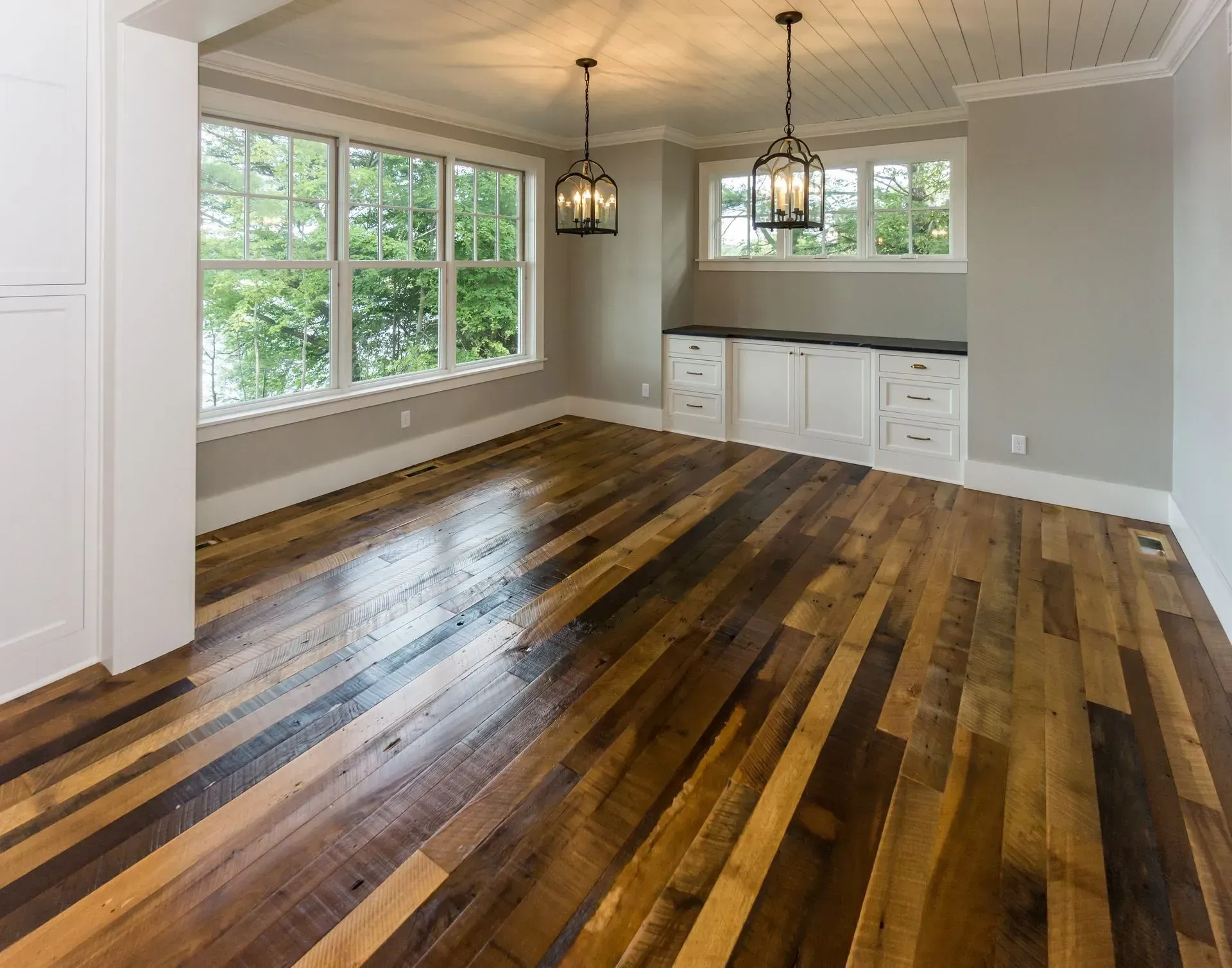 Room with wood flooring, large windows, white cabinets, and two hanging black lanterns.