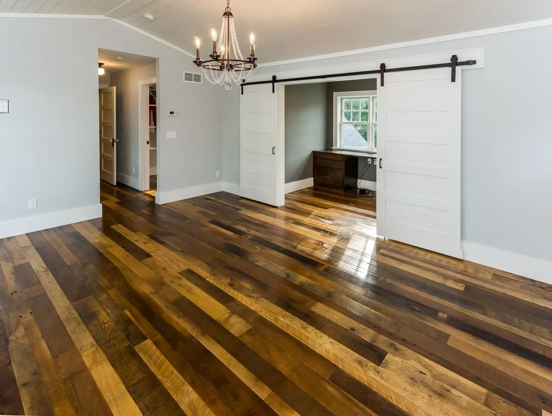 Room with hardwood floor, sliding barn doors, gray walls, chandelier, and a desk.