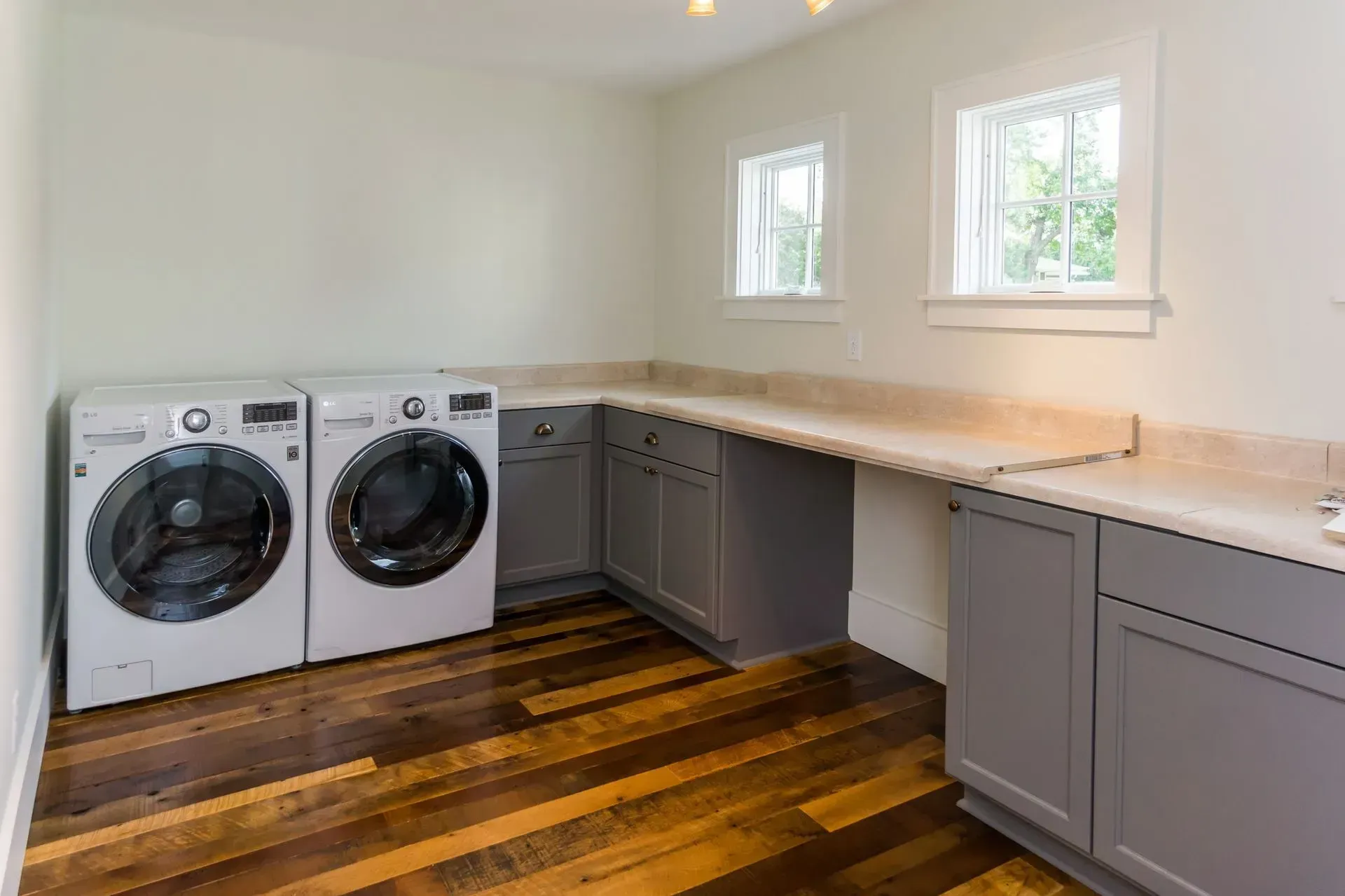 Laundry room with washer, dryer, gray cabinets, countertop, and hardwood floor.