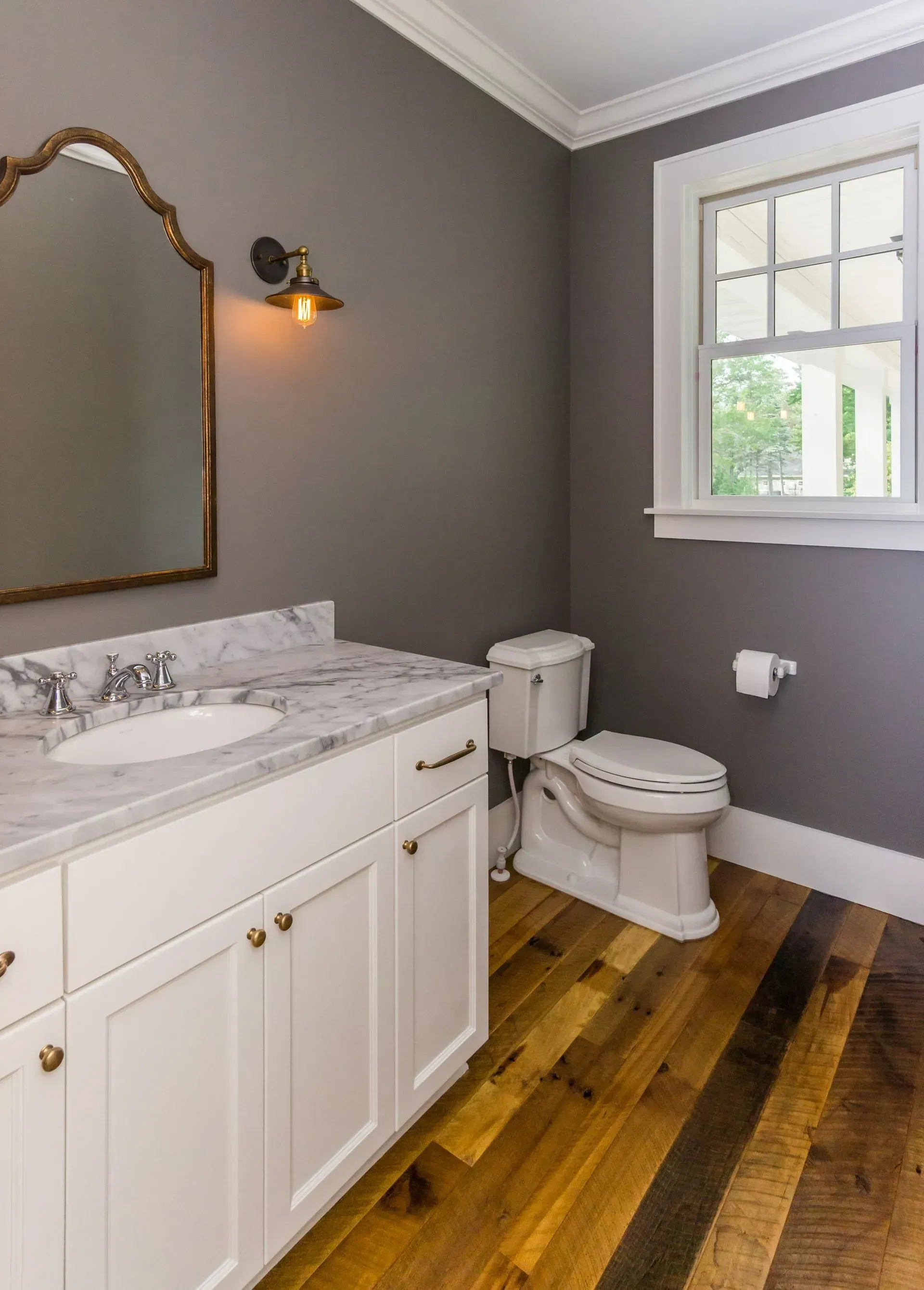 Bathroom with white vanity, marble countertop, wooden floor, gray walls, and window.