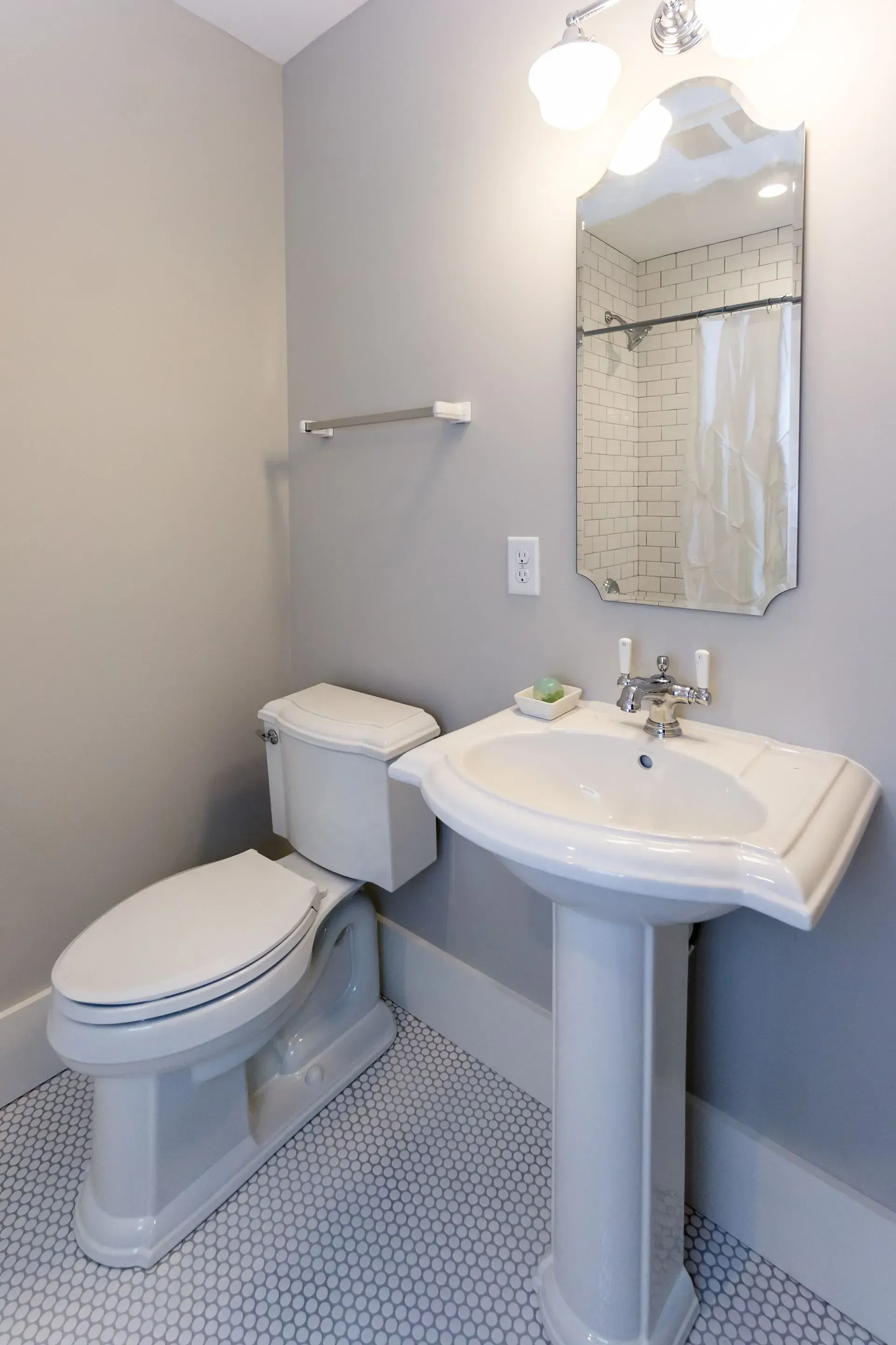 Bathroom with white toilet and pedestal sink, gray walls, and patterned floor.