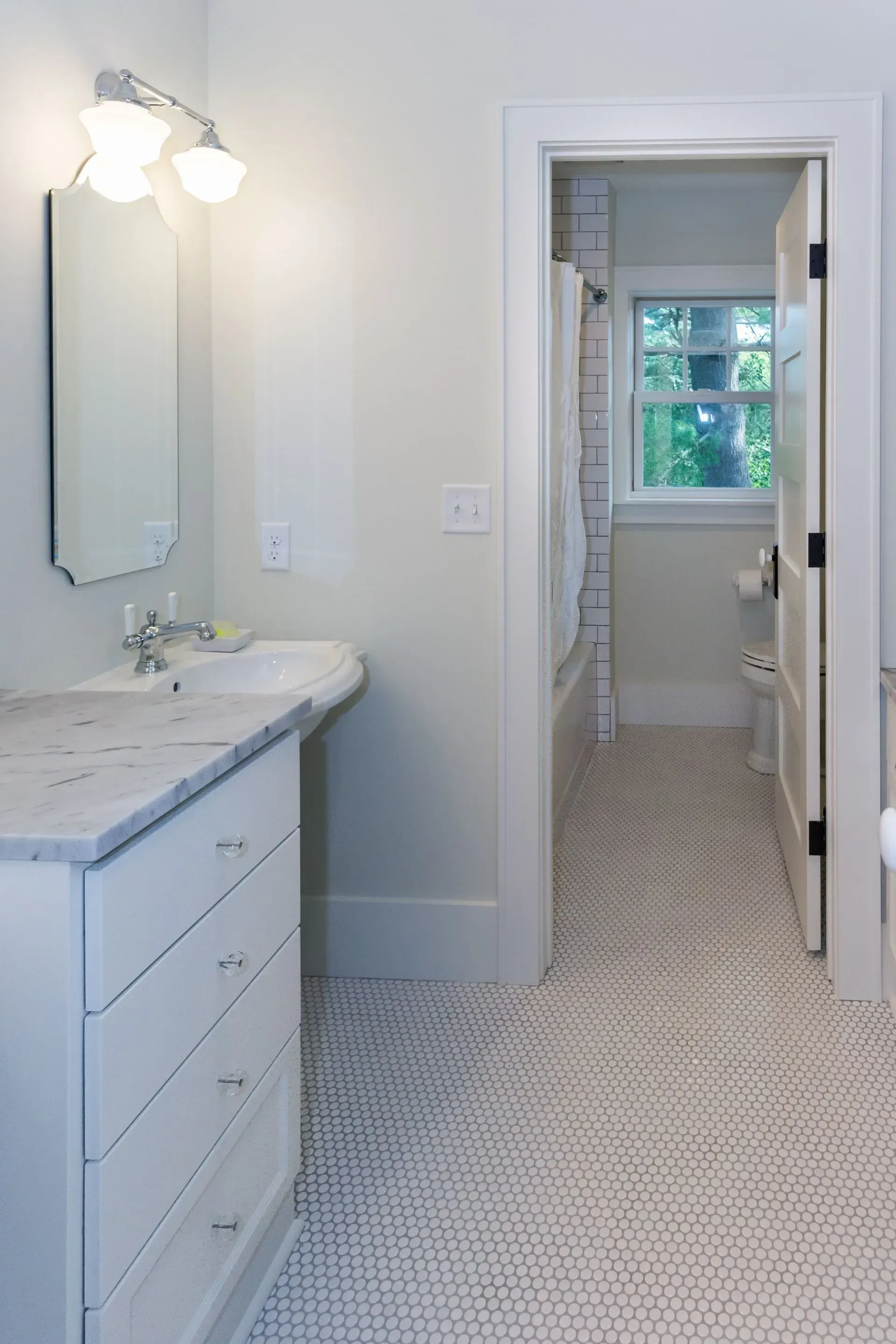 White bathroom with marble countertop, drawers, and open door to tub/shower area.