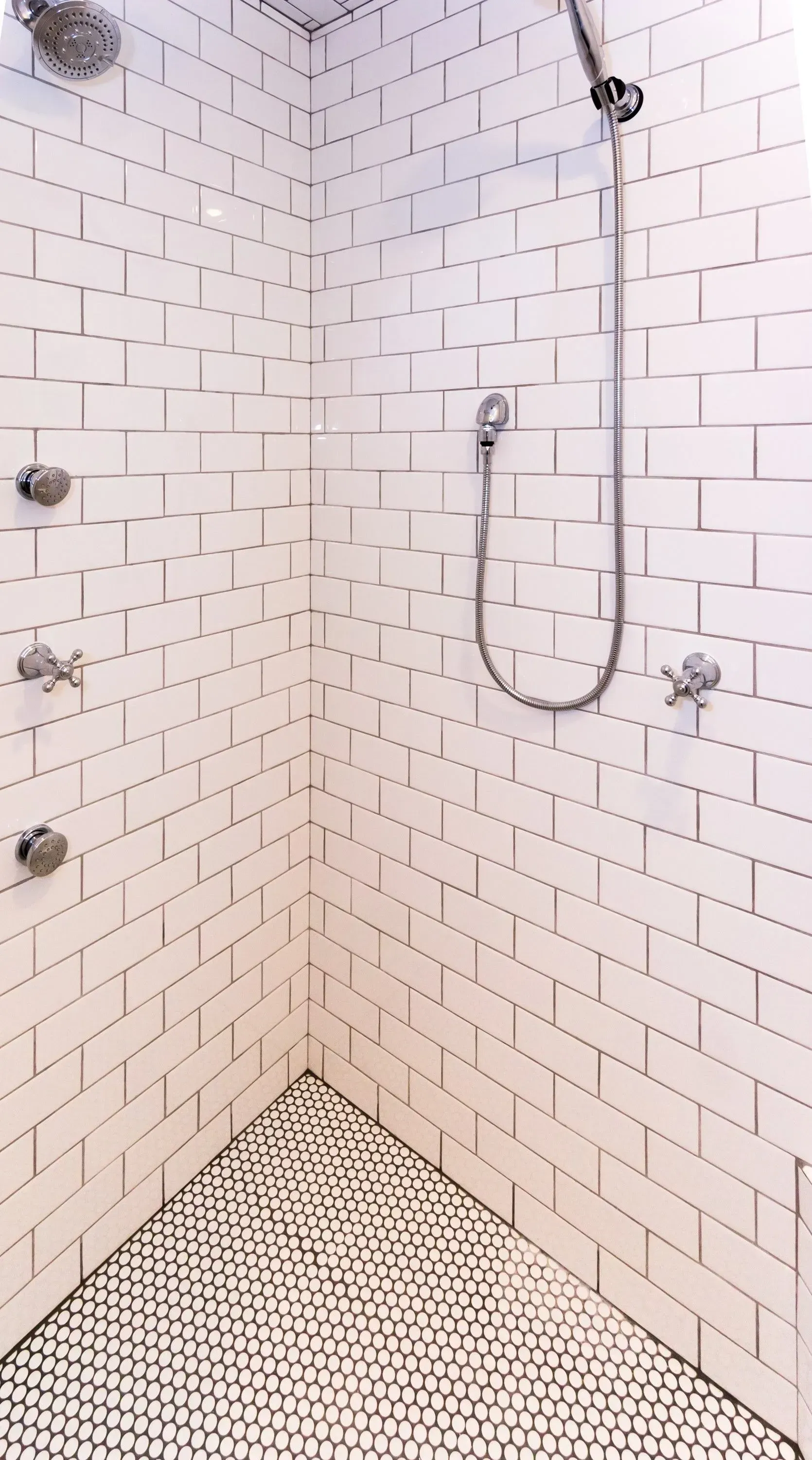 White tiled shower with black and white mosaic floor, silver fixtures, corner view.