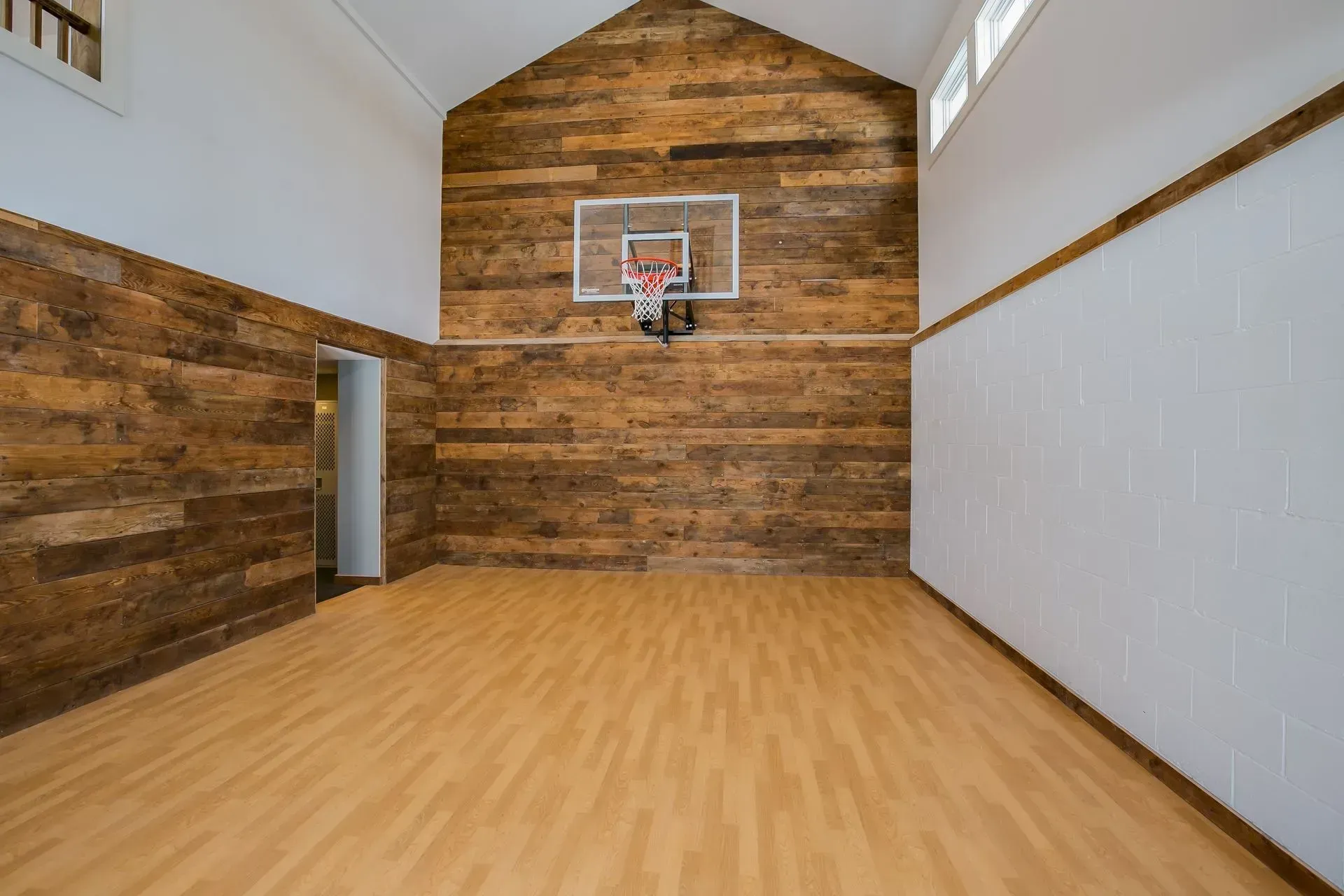Empty indoor basketball court with wooden accent wall, hoop, and light wooden floor.