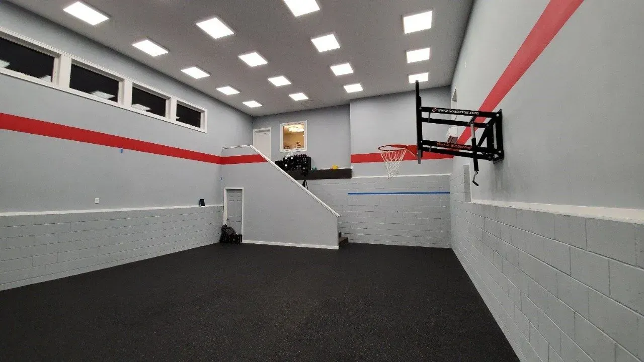 Gym with a basketball hoop on the wall, gray walls with red stripes, black floor.