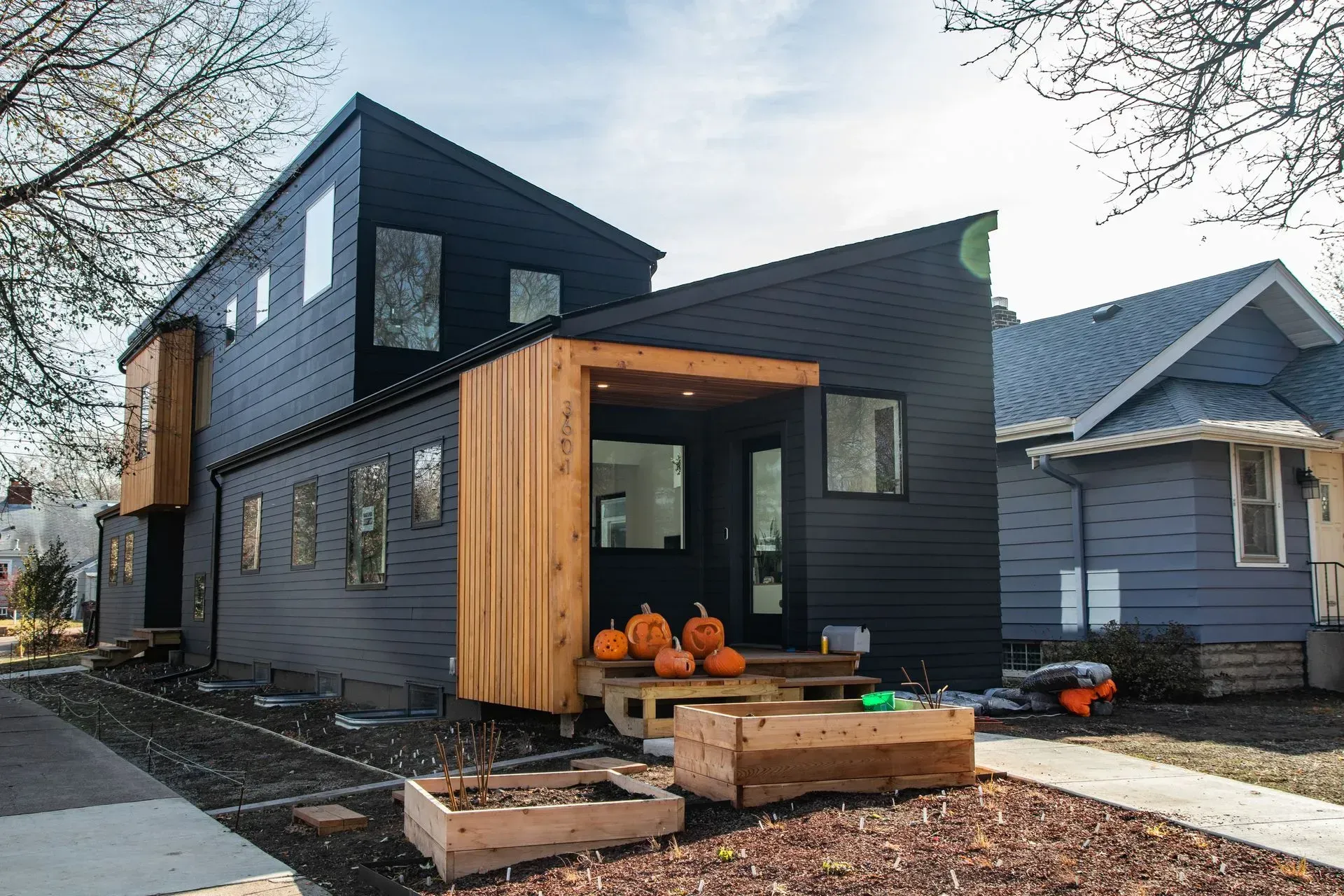 Modern black house with wooden accents; pumpkins and planters on the front porch.