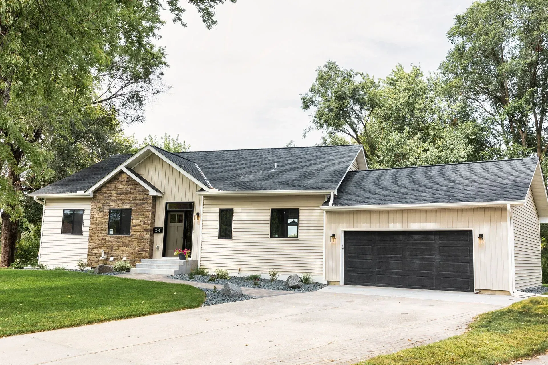 Modern home with tan siding, stone accent, and attached garage; overcast sky.