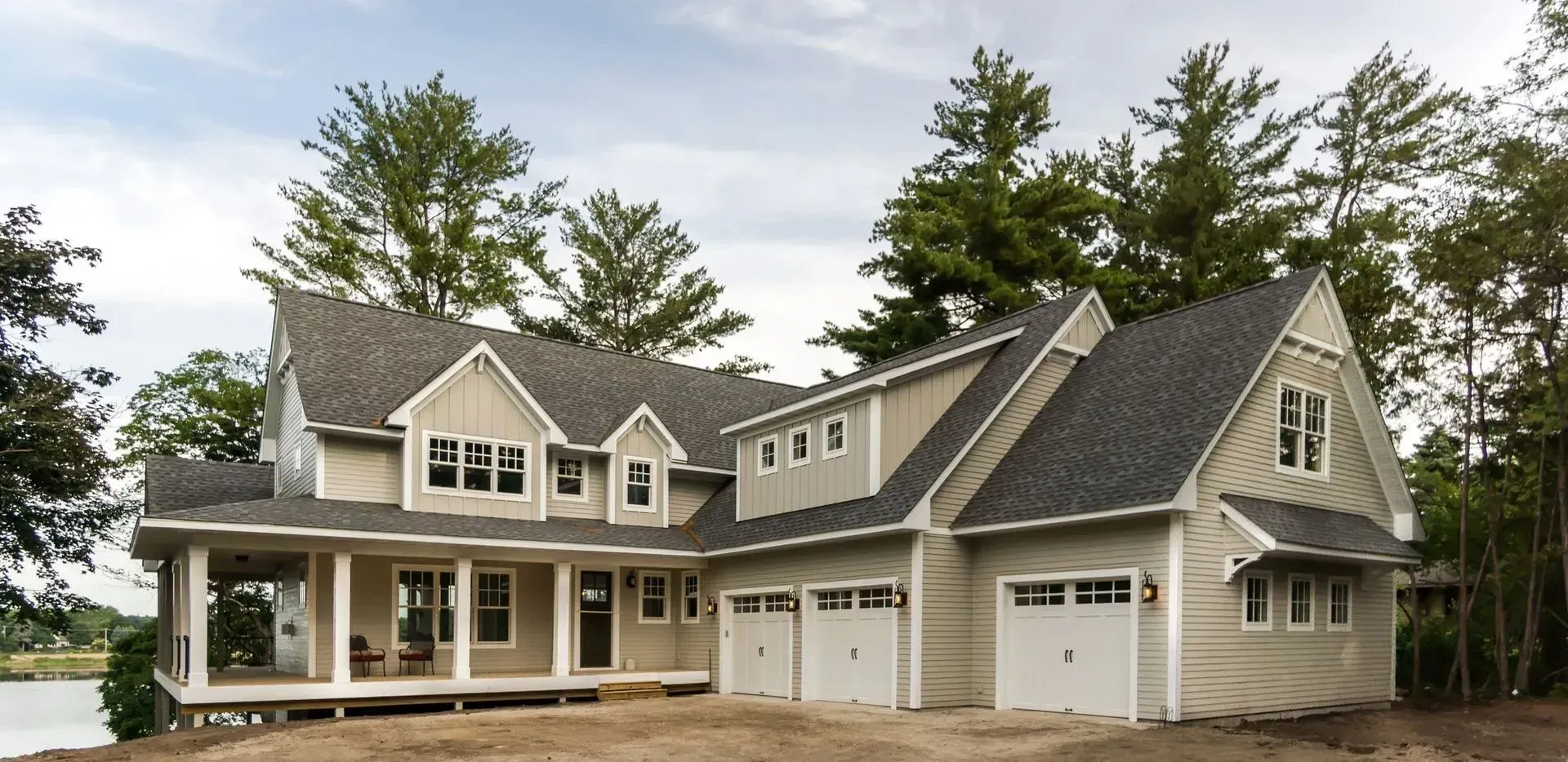 A large, two-story house with a porch and three-car garage. Overlooking water, surrounded by trees.