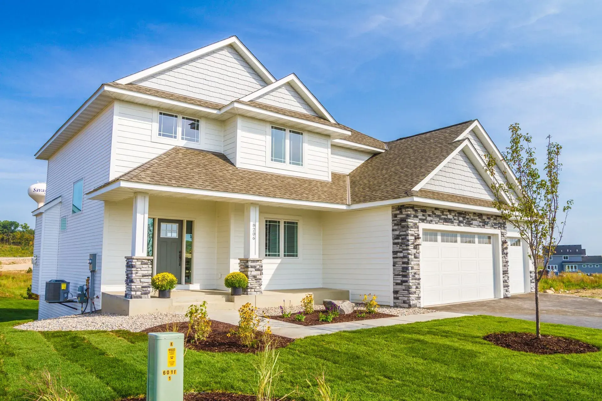 White two-story house with brown roof and gray stone accents. Green lawn and blue sky.