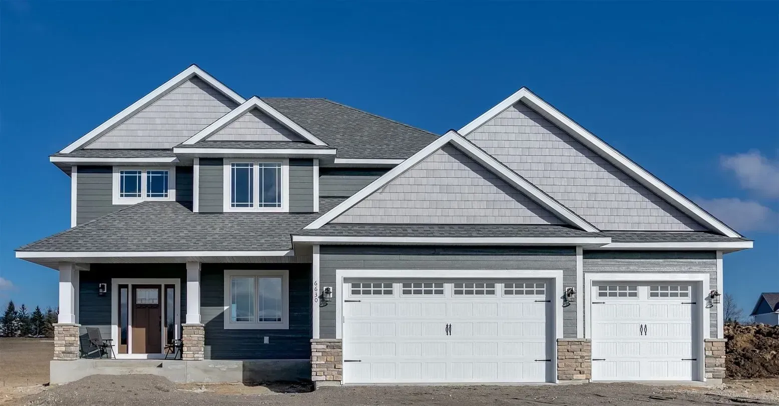Two-story gray house with white trim, a three-car garage, and a blue sky.