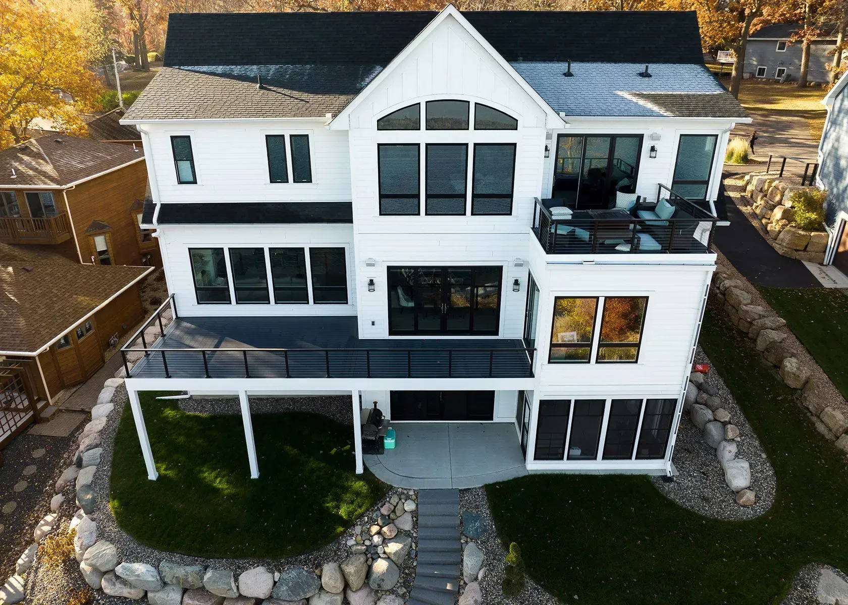 White modern house with multiple decks, overlooking a landscape with rocks and green grass.