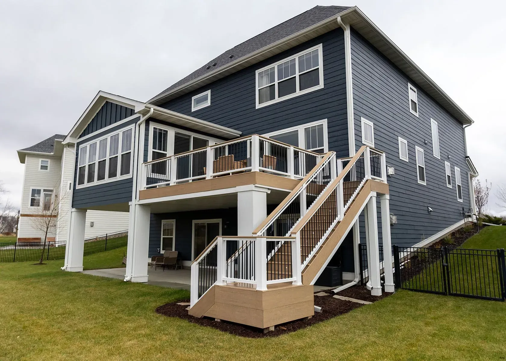 Two-story house with a deck and enclosed porch. Blue siding, white trim, and a grassy backyard.