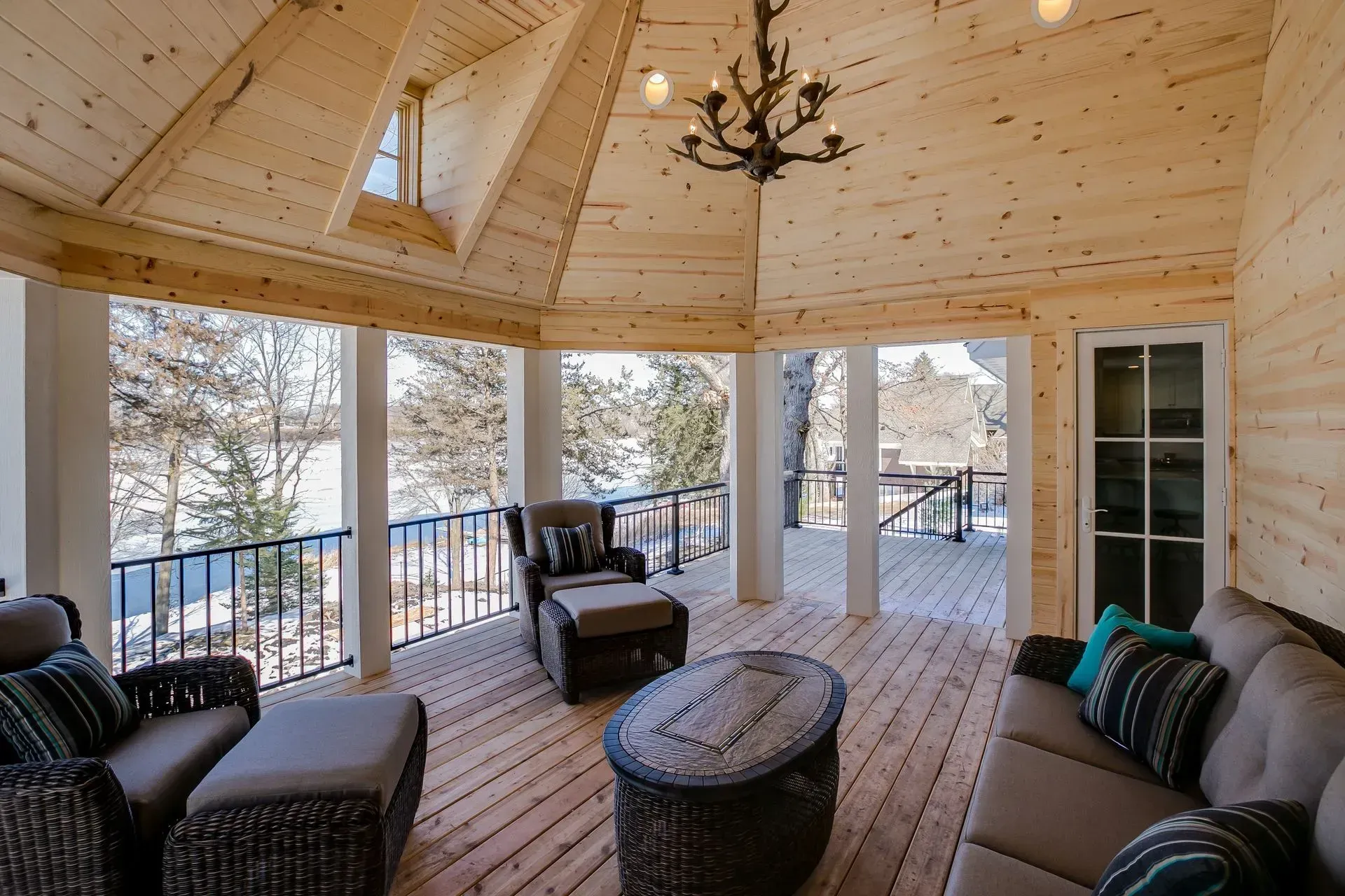 Enclosed porch with wood paneling, seating, and a view of a lake.