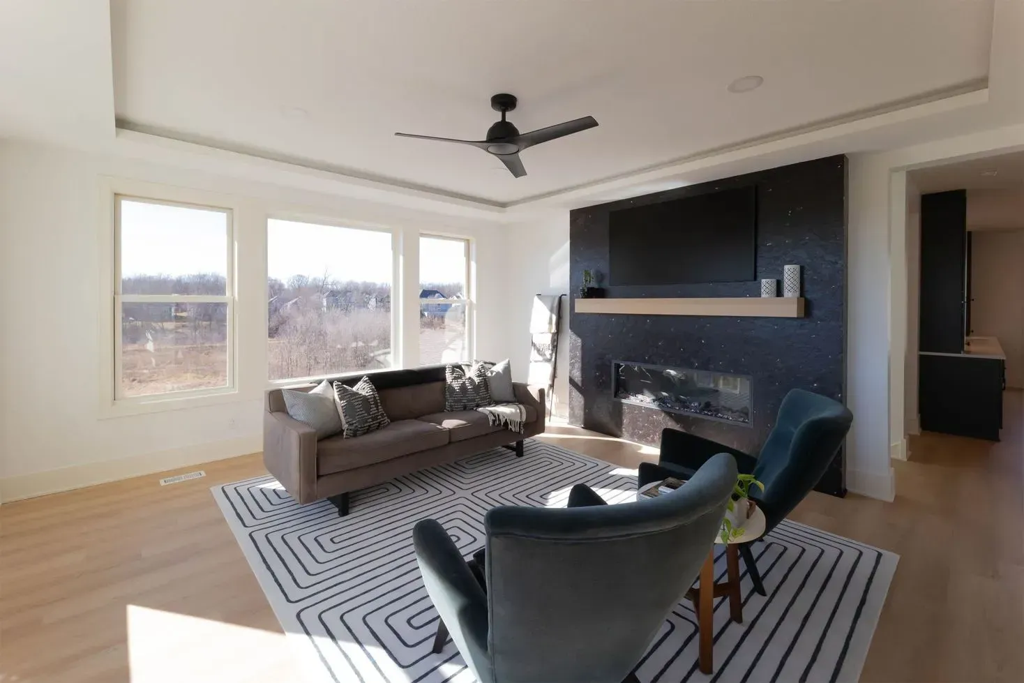 Living room with sofa, two blue chairs, fireplace, and large windows.