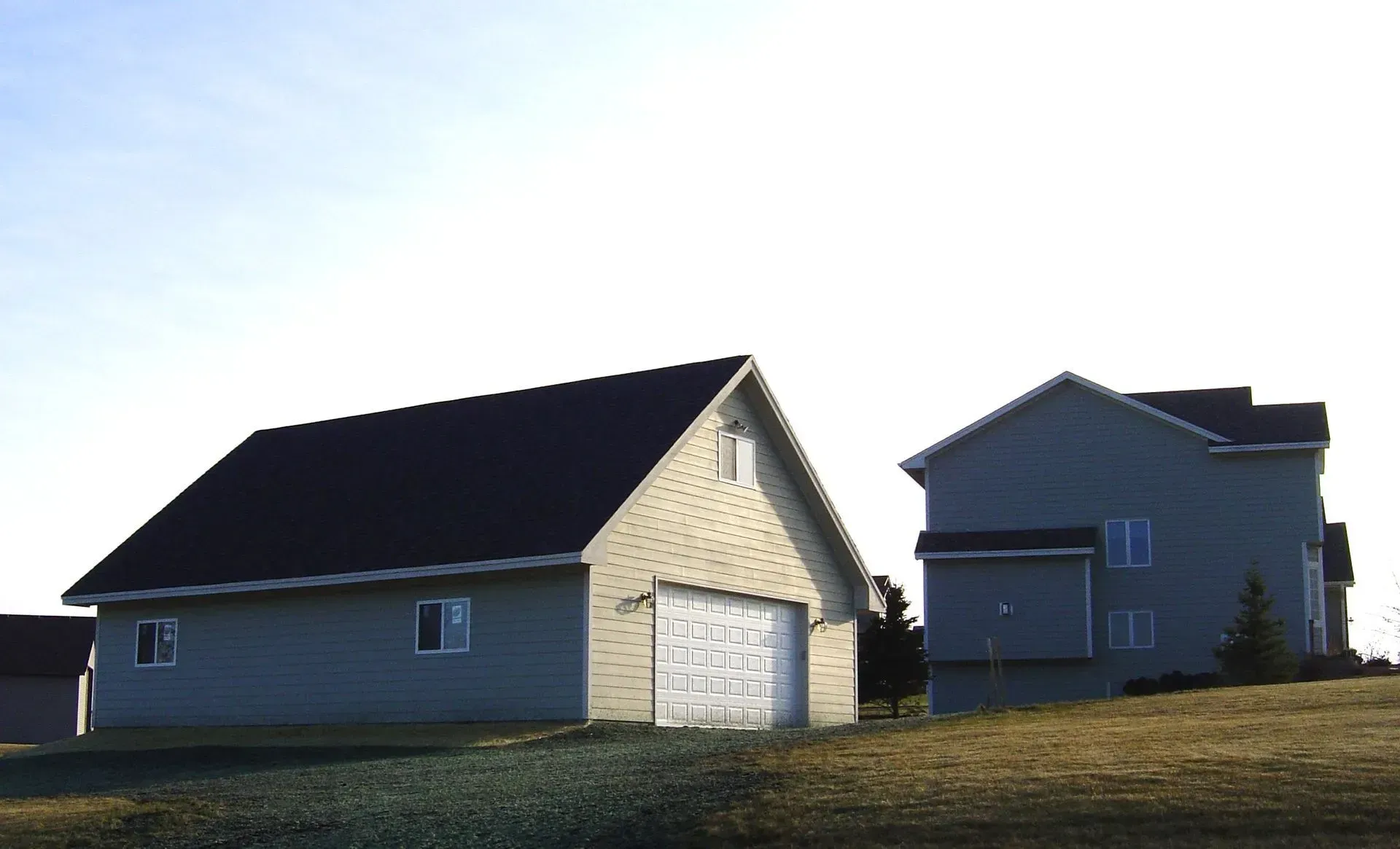 Tan garage and two-story house on a grassy hill, under a clear sky.