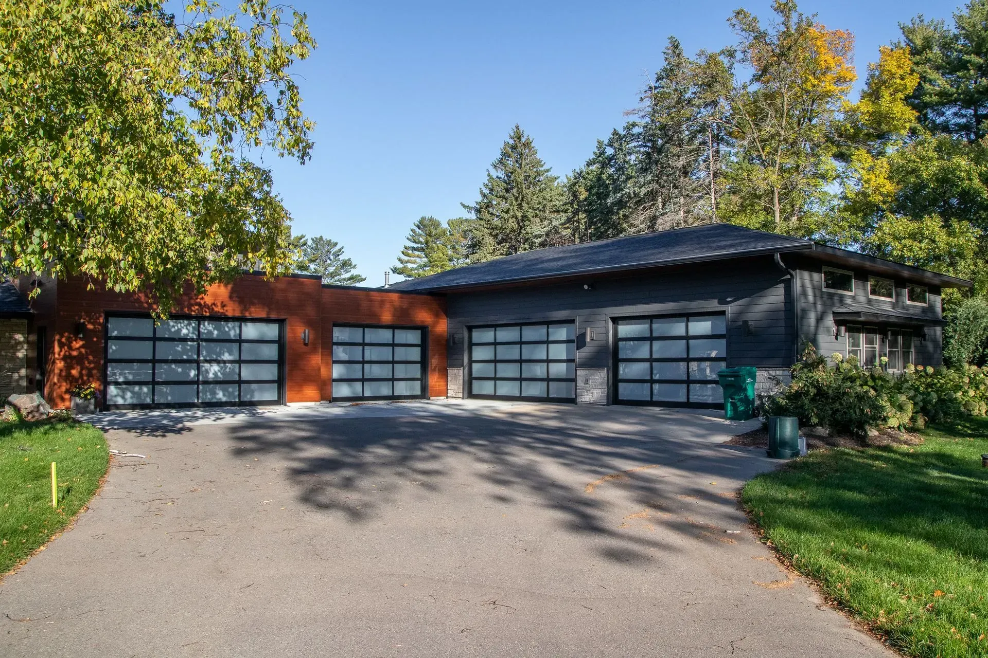 House exterior with three garage doors, one orange and two black, driveway, trees, and blue sky.