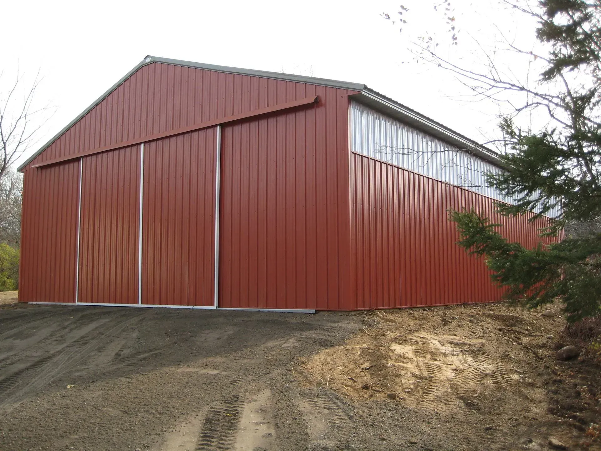 Red metal barn with sliding doors on dirt driveway.