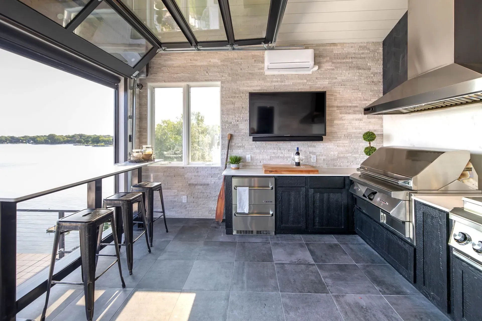 Outdoor kitchen with grill, bar, and TV, overlooking a lake.
