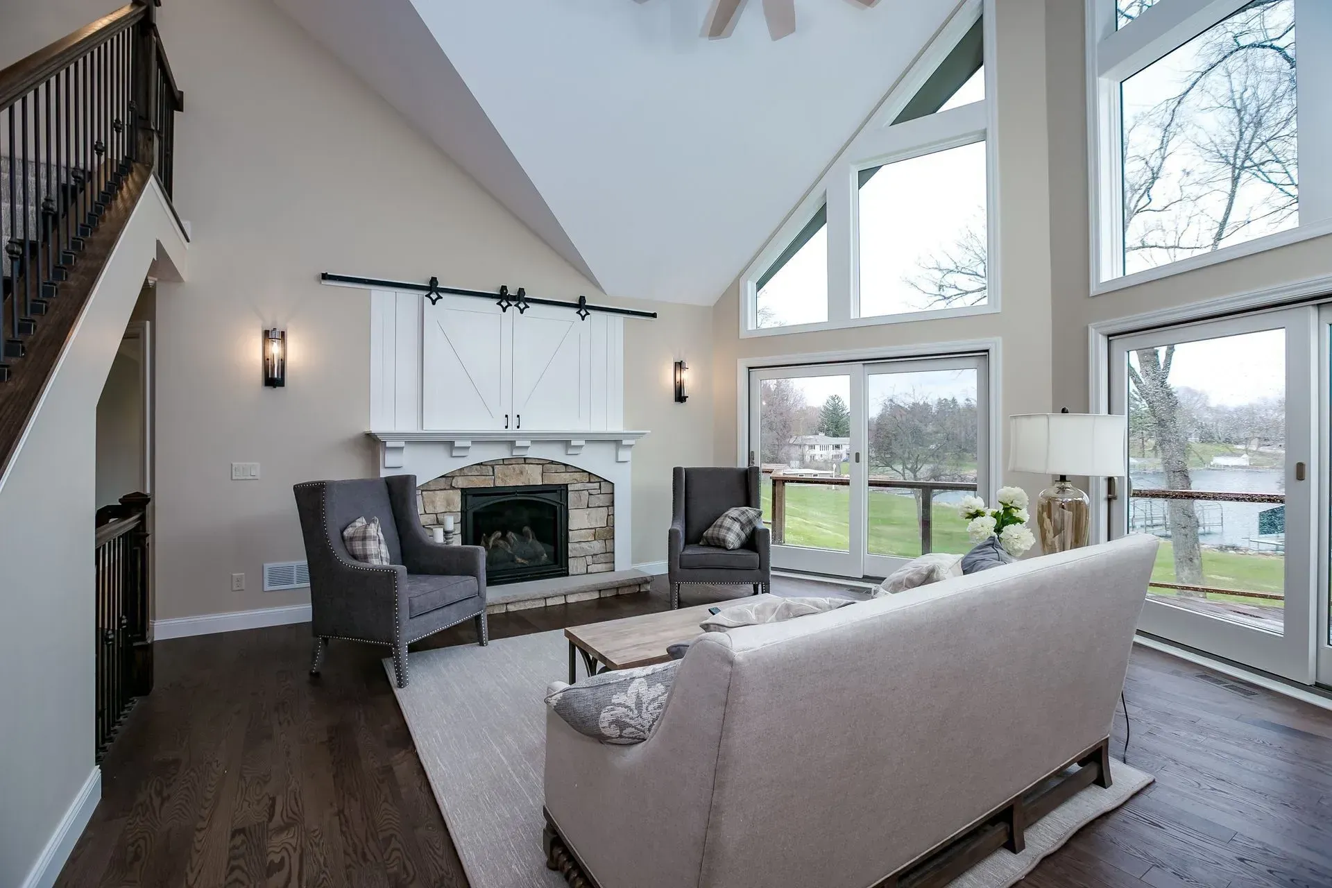 Living room with fireplace, vaulted ceiling, large windows overlooking a green lawn.