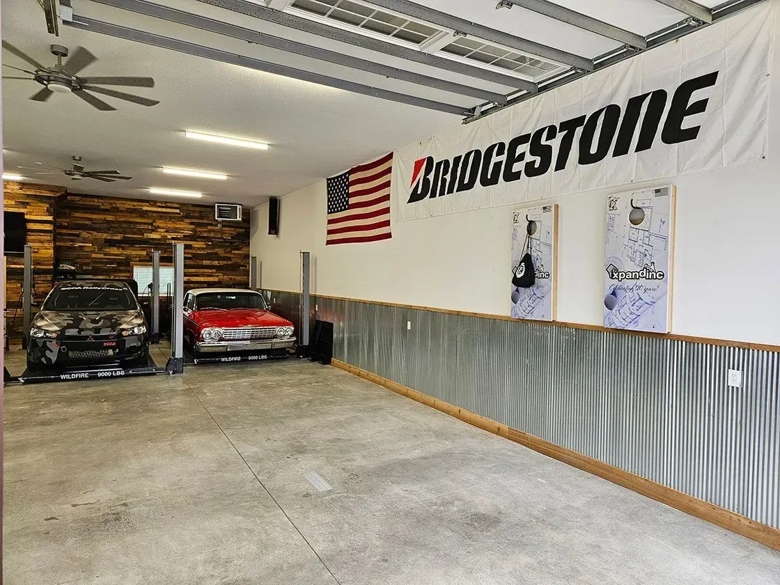 Garage interior with cars on lifts, American flag, Bridgestone banner, corrugated metal wall.