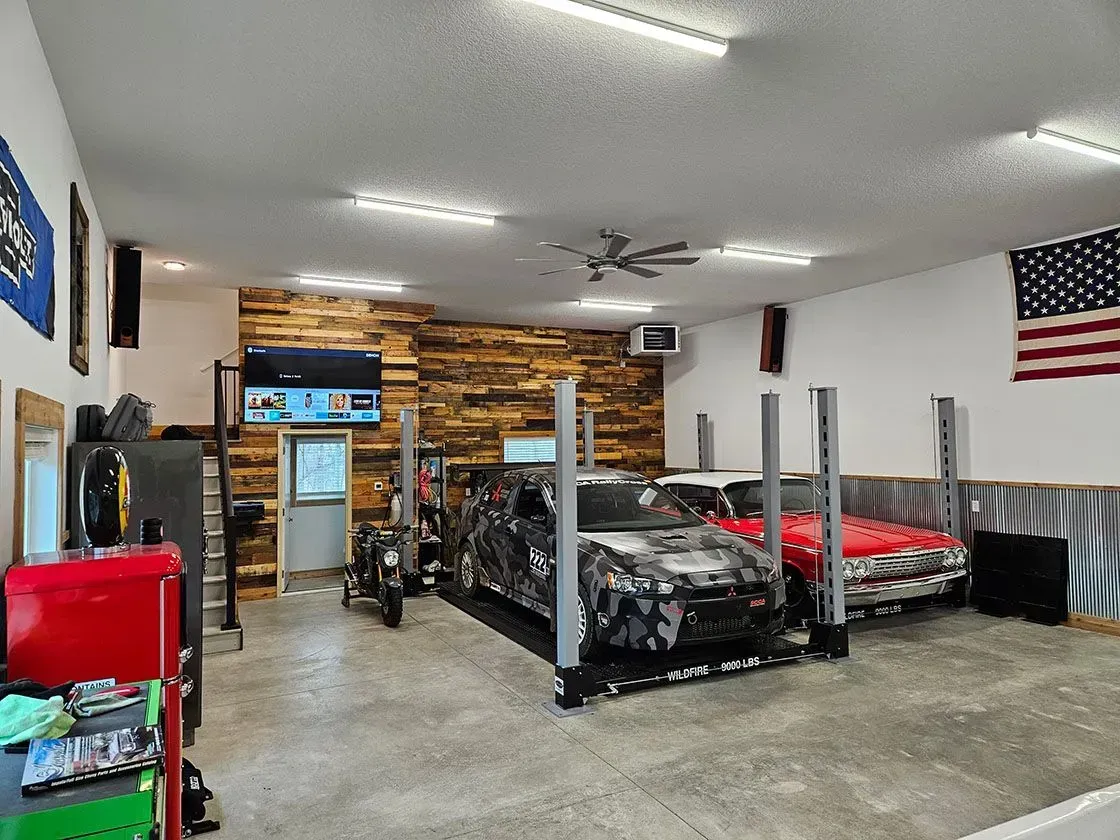 Garage interior with vehicles on lifts, TV, wood accent wall, and American flag.