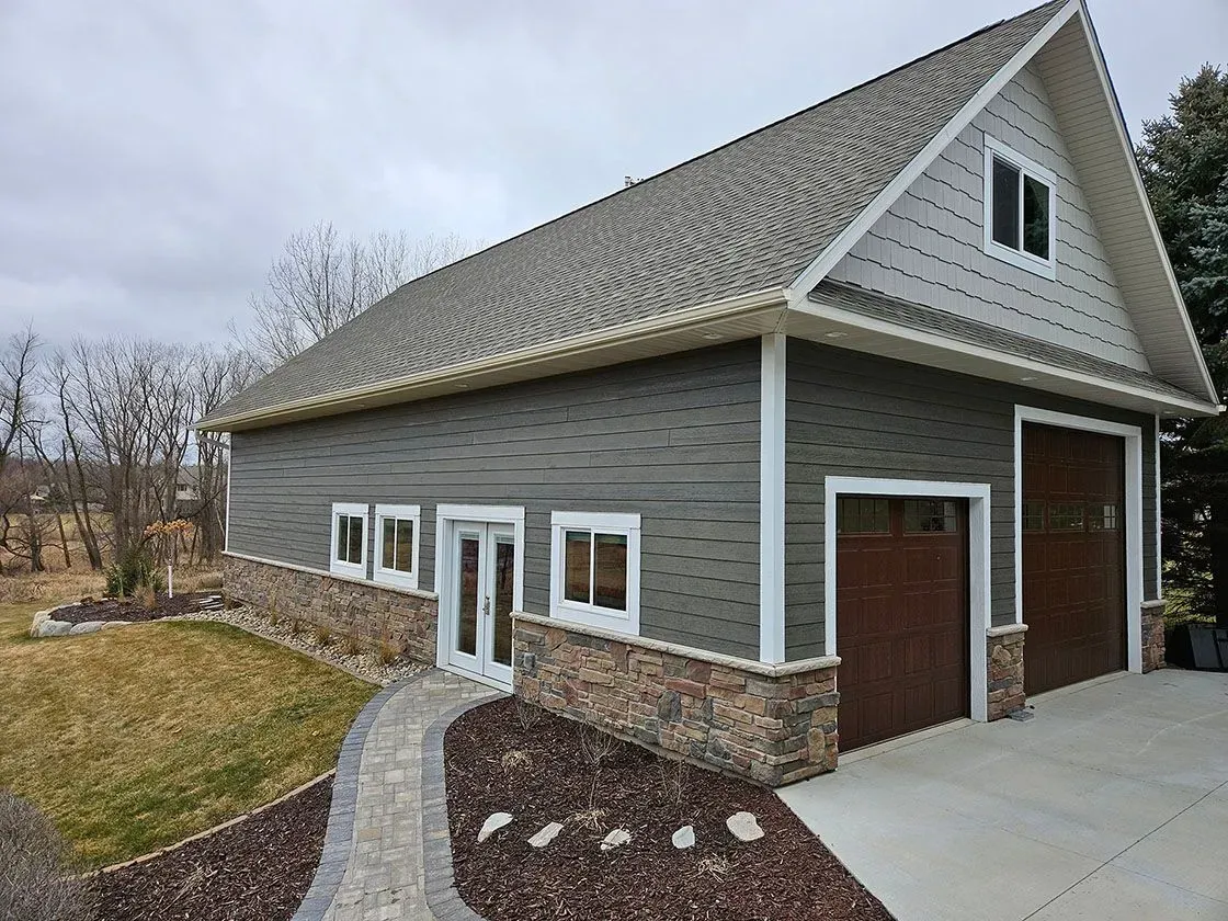 Two-story gray building with brown garage doors, stone accents, and a stone pathway leading to the entrance.