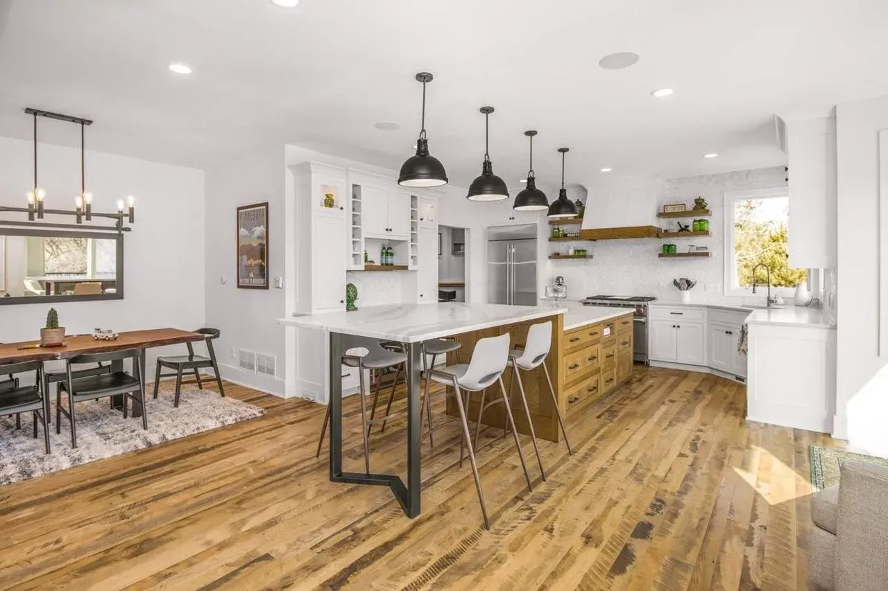 Bright, modern kitchen with island, pendant lights, wooden floor, and dining area.