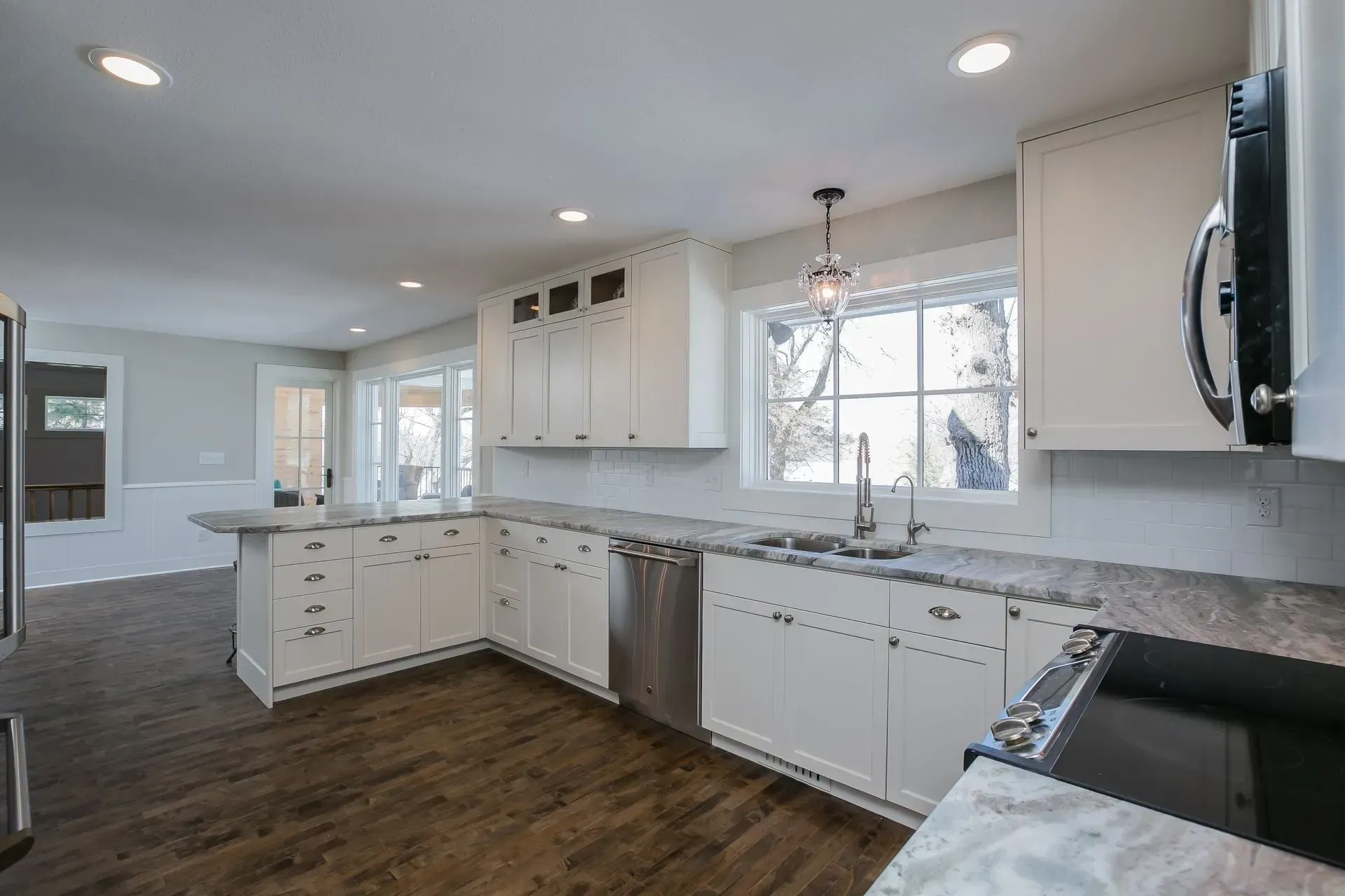 White kitchen with stainless steel appliances, marble countertops, and dark wood floors.
