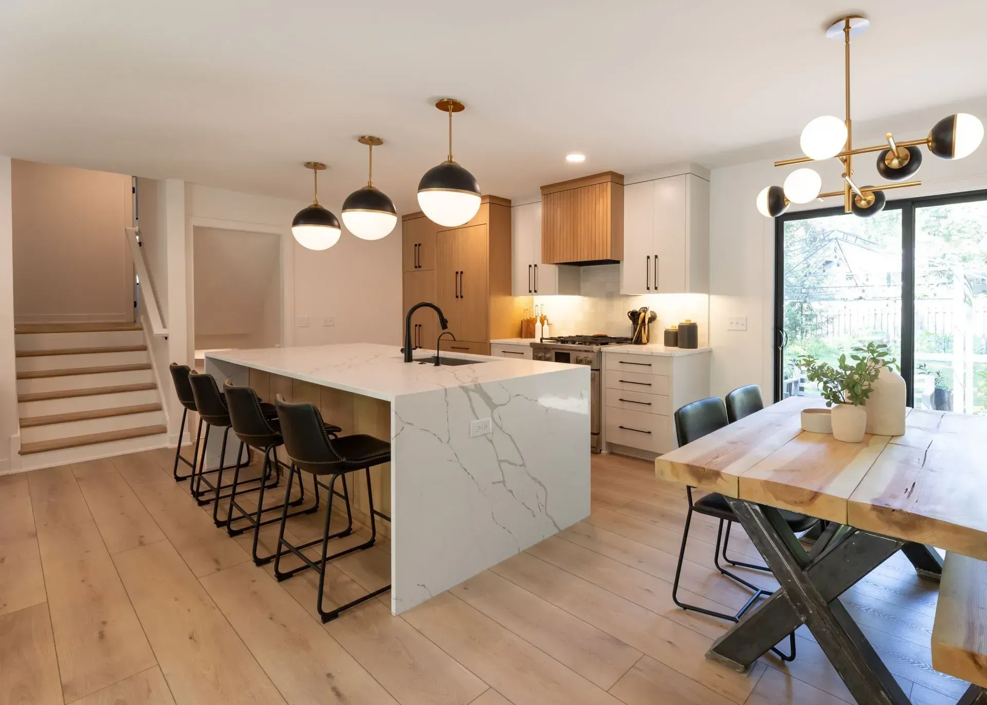 Modern kitchen with island, seating, and dining table; white and wood tones; black accents.