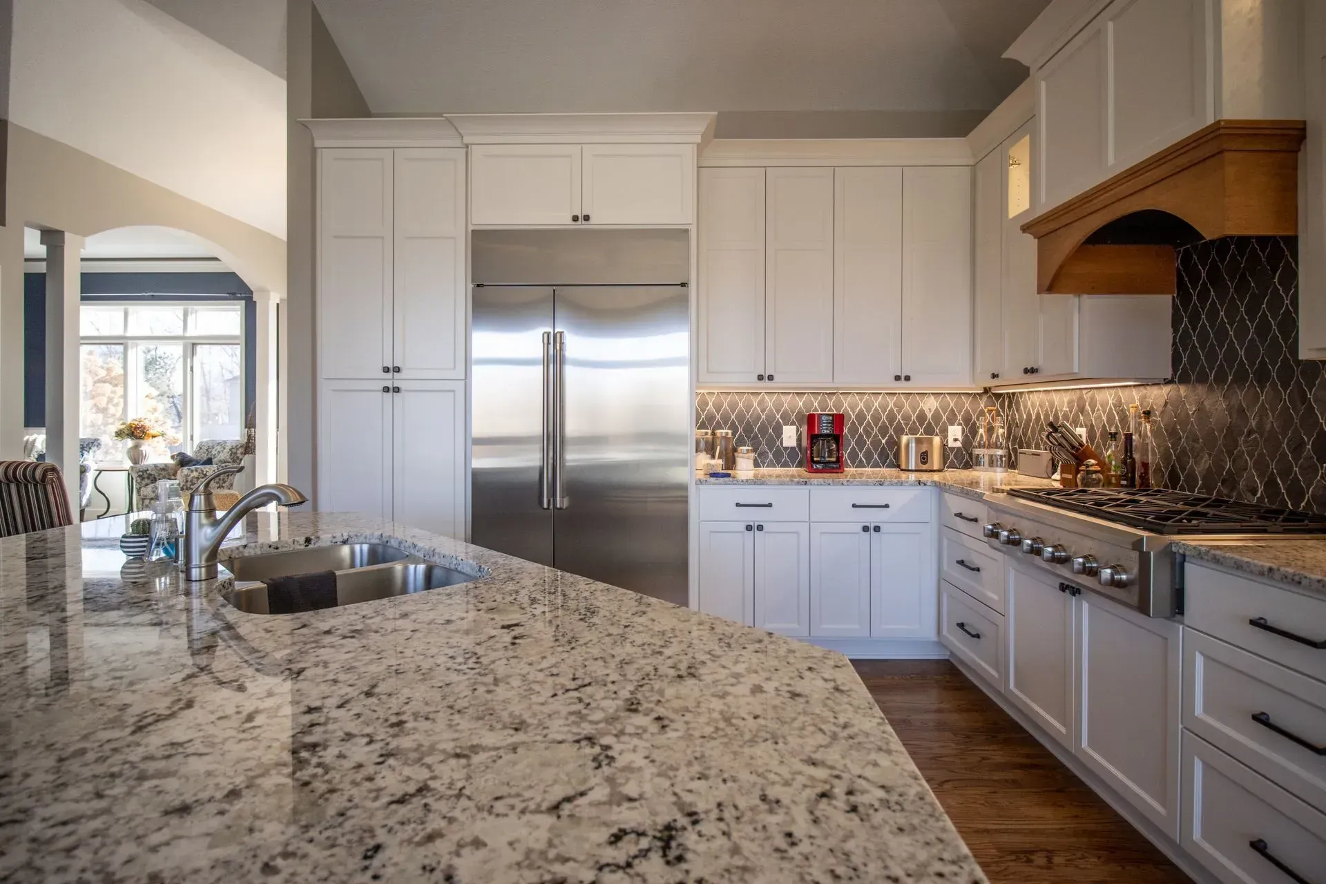 White kitchen with granite countertops, stainless steel appliances, and wood range hood.