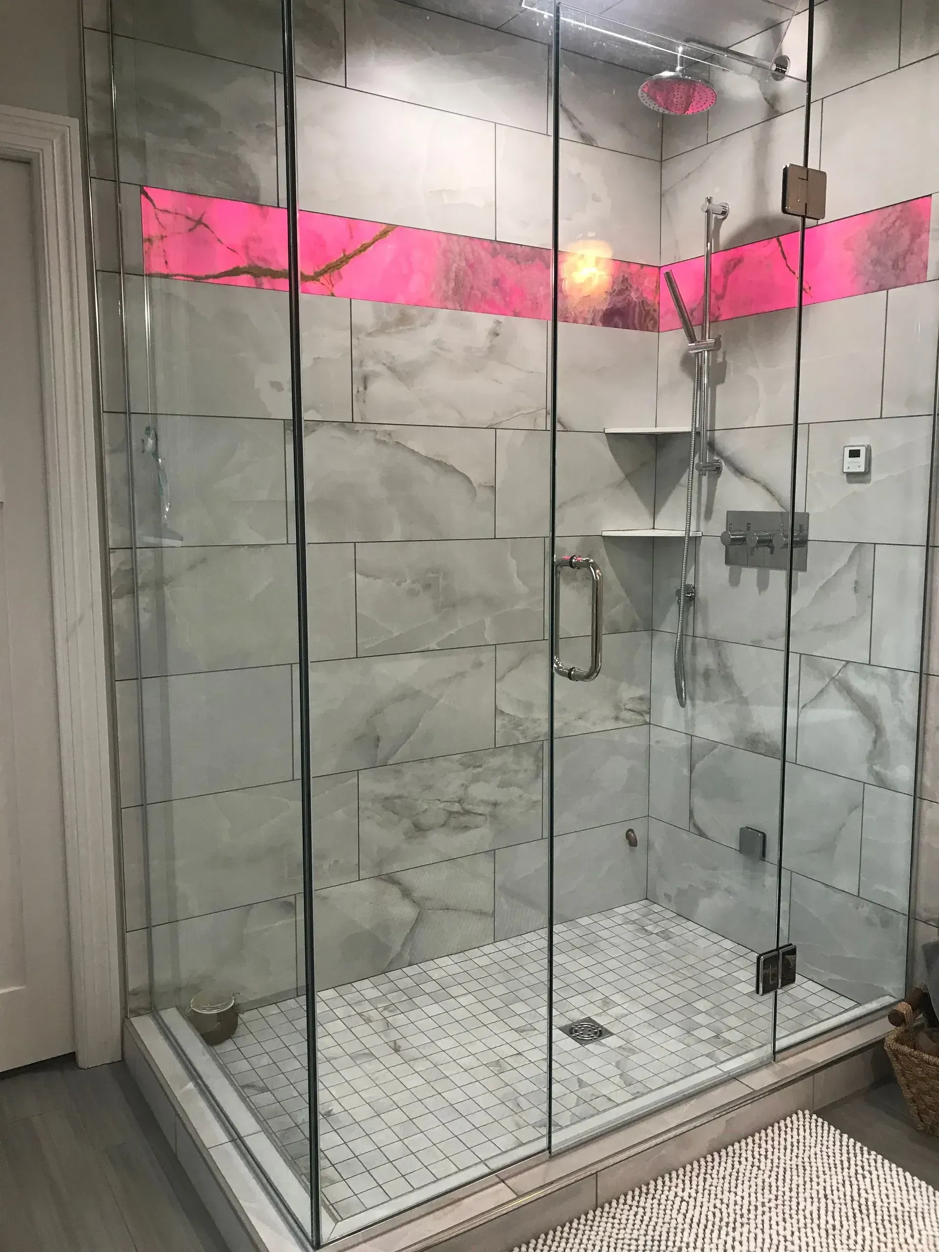Glass shower enclosure with gray marble tile, pink accent, and chrome fixtures.
